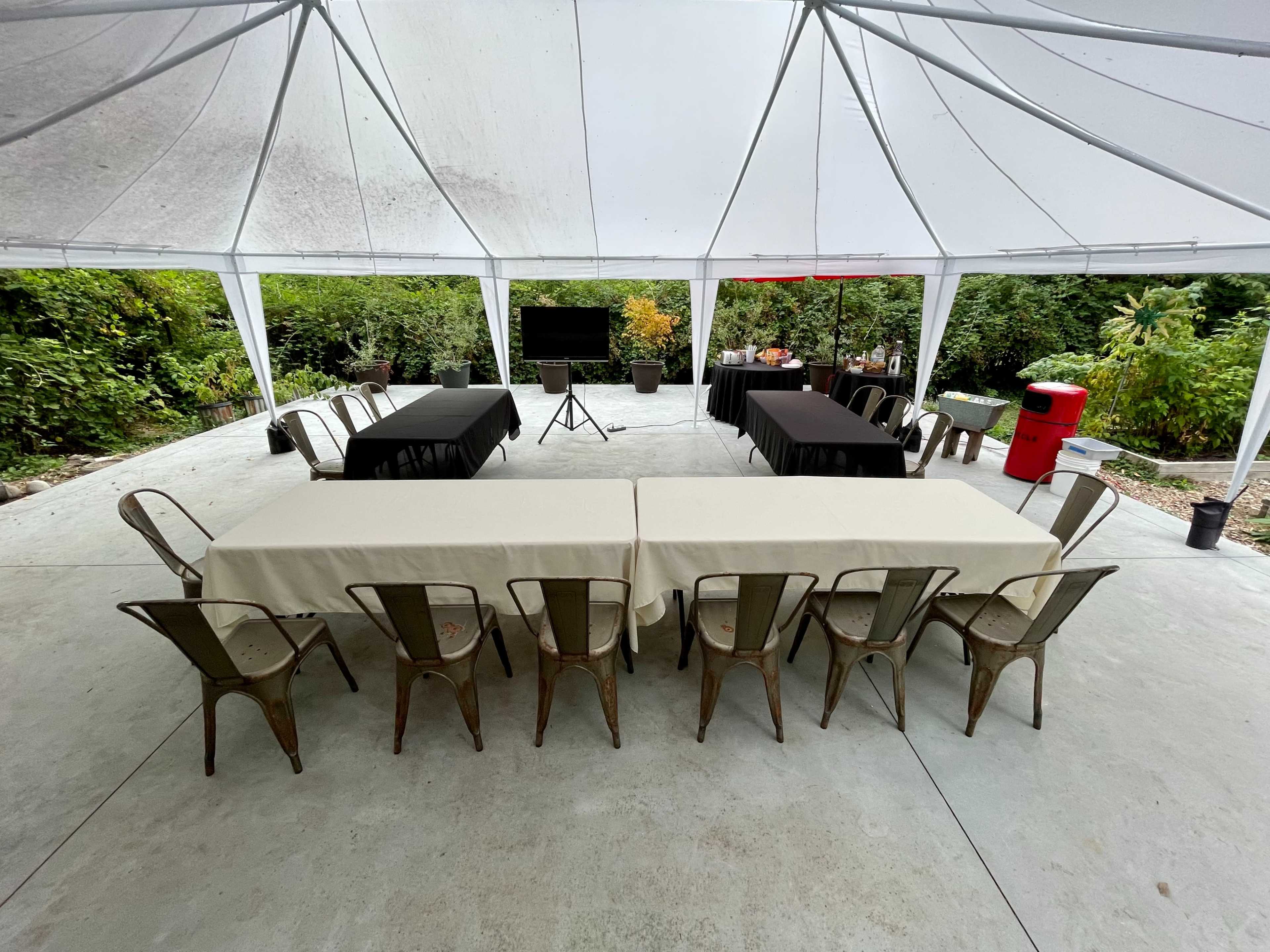 A large outdoor tent features several tables arranged in a U-shape, with black and beige tablecloths set on the tables.