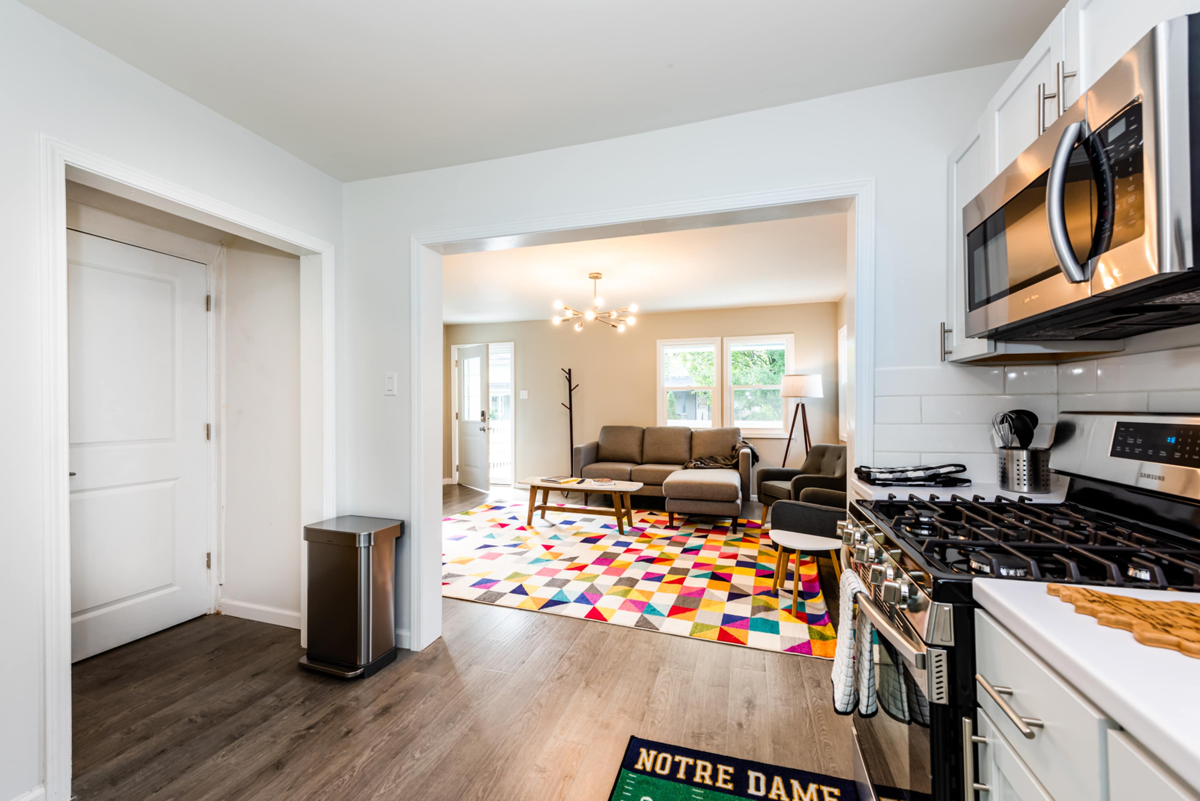 A modern kitchen that opens into a living room featuring a colorful patterned rug and a seating area.