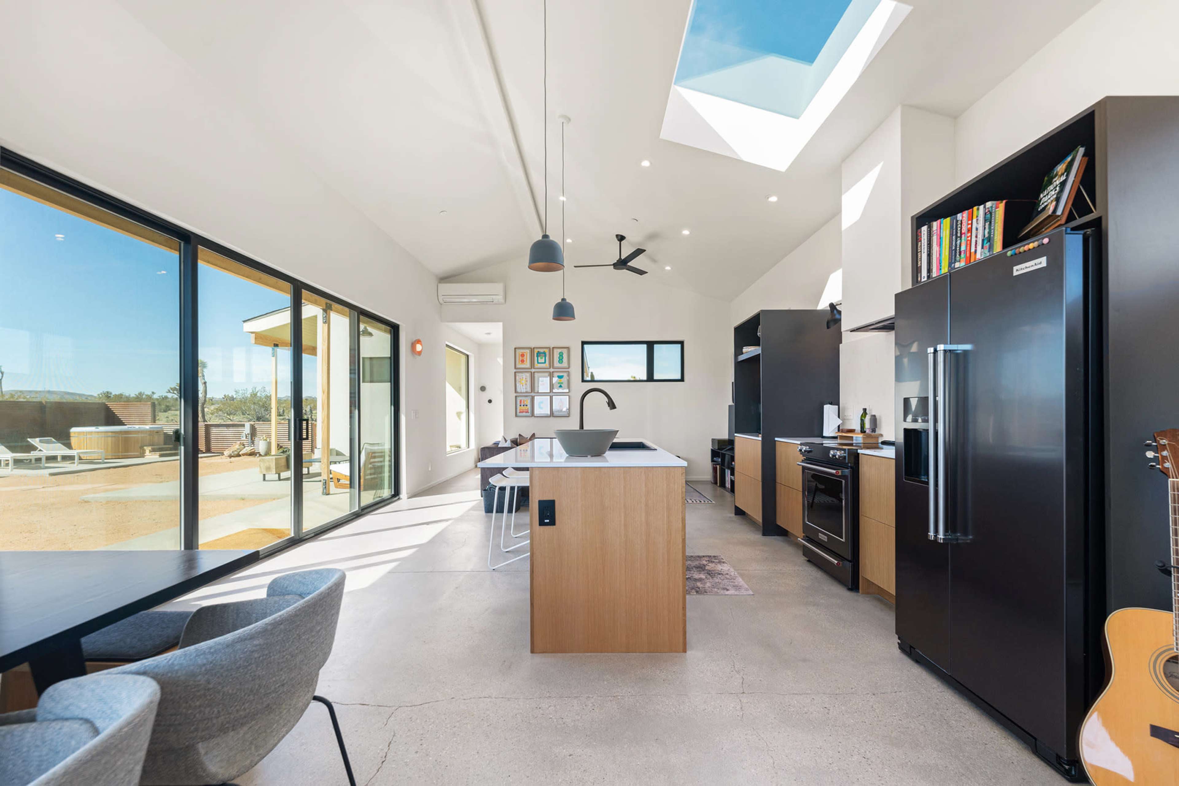 A modern, open-concept kitchen and dining area with large windows, a skylight, and sleek black appliances.