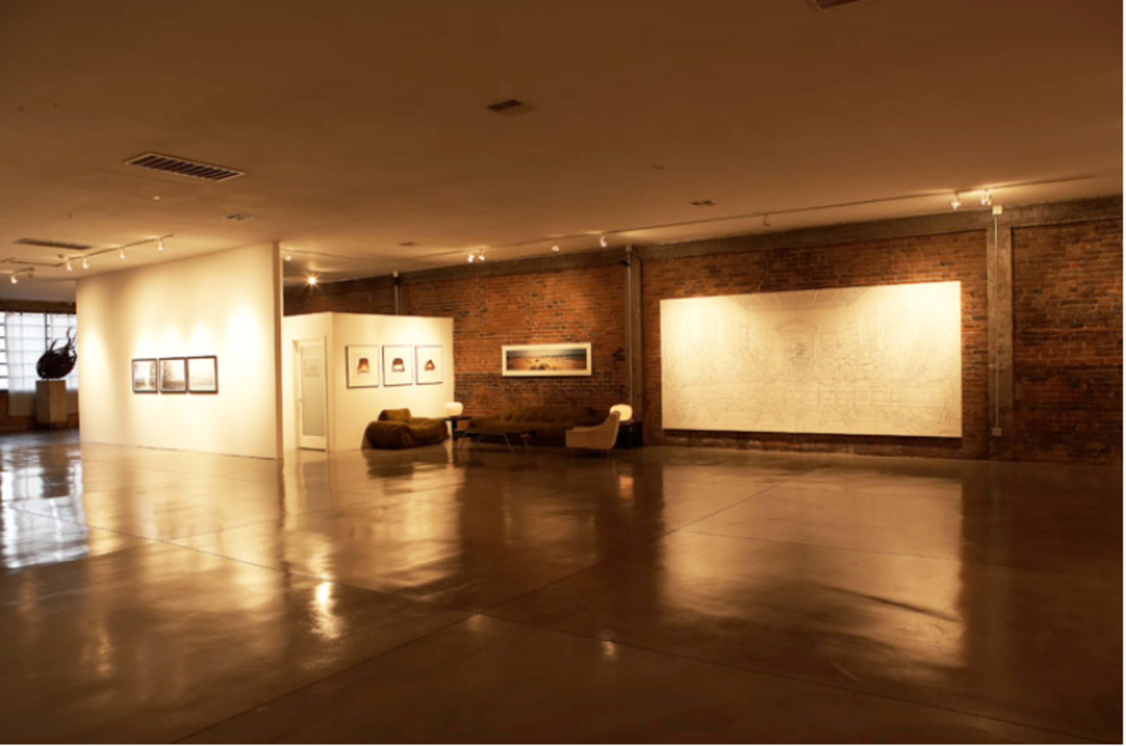 An art gallery with exposed brick walls, polished concrete floors, and mounted artworks on display.