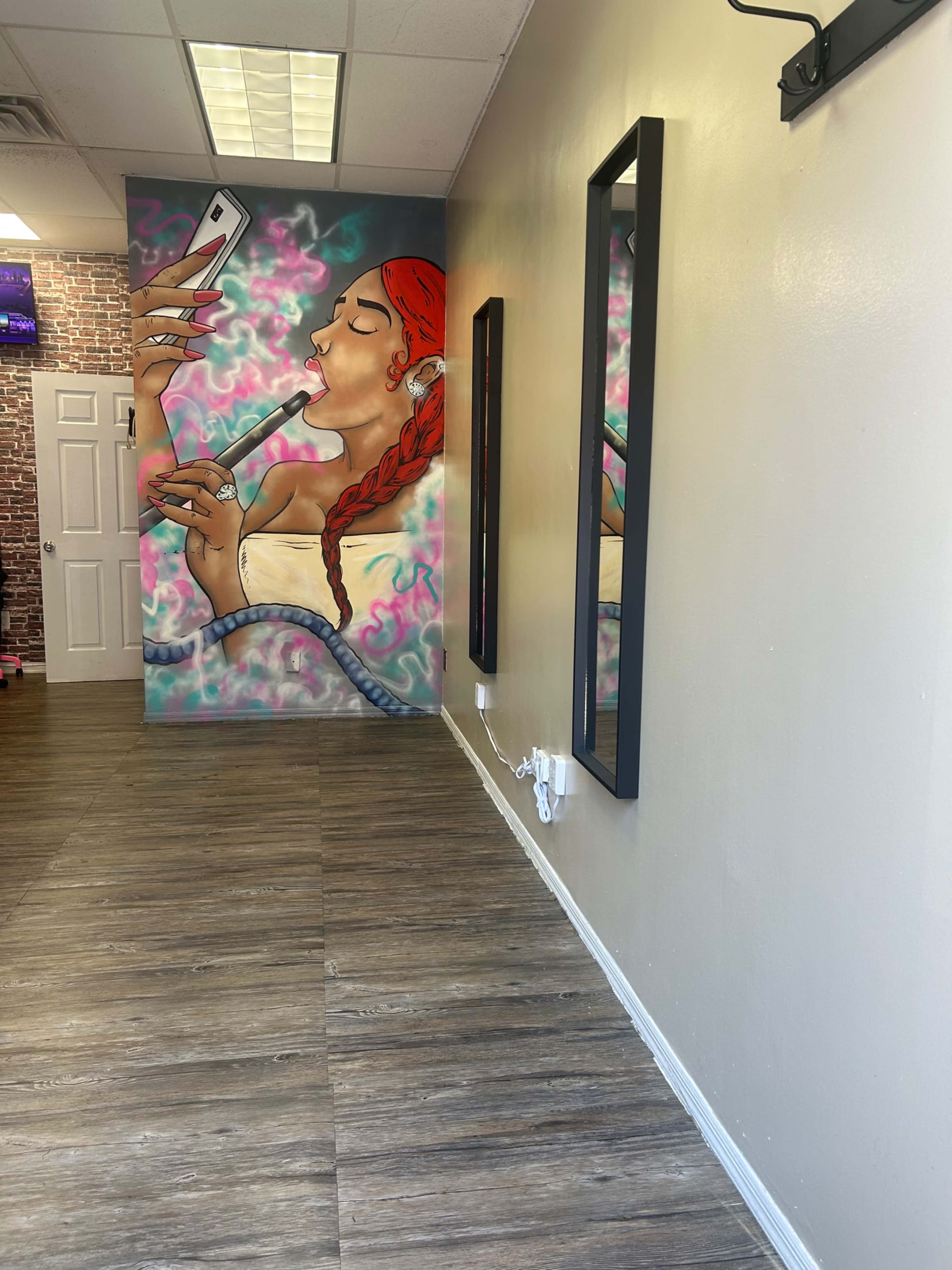 The image shows a stylish interior with a mural of a woman holding a phone and a hookah on one wall, complemented by two black mirrors on the opposite wall.