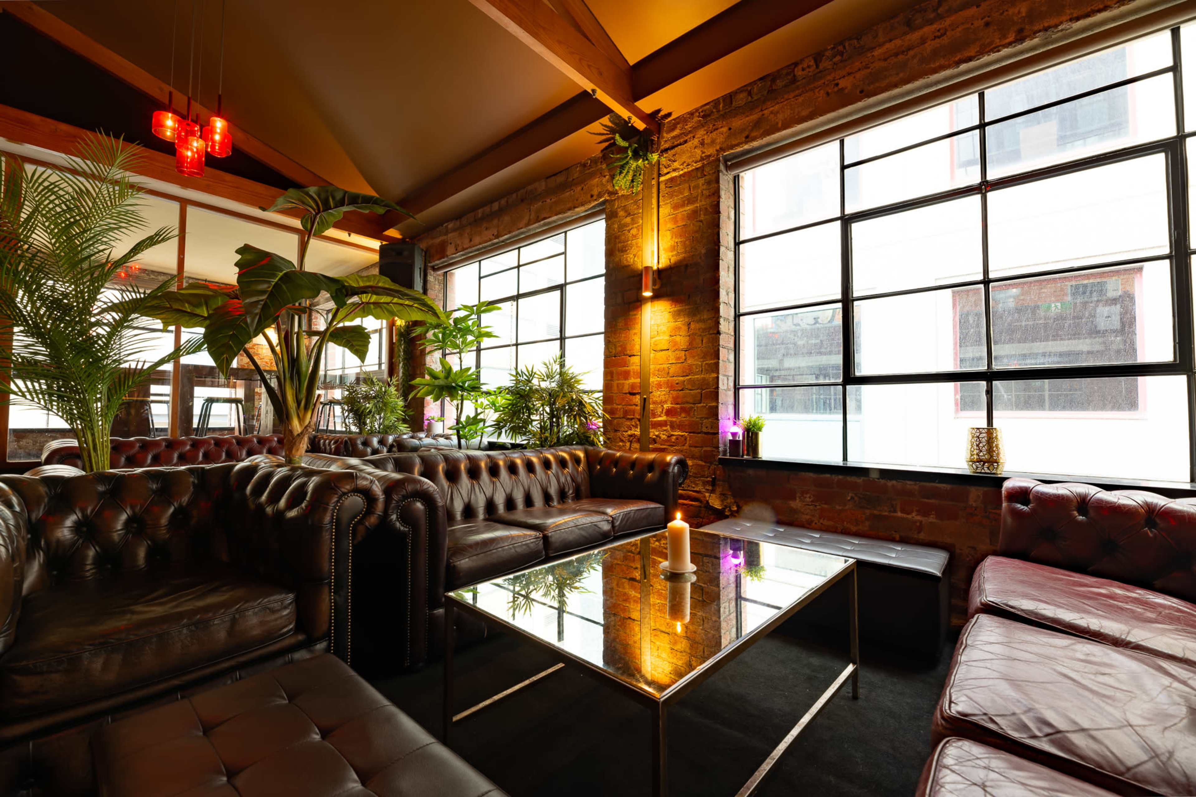 A cozy lounge area features leather sofas, vibrant plants, and large windows allowing natural light to fill the space.