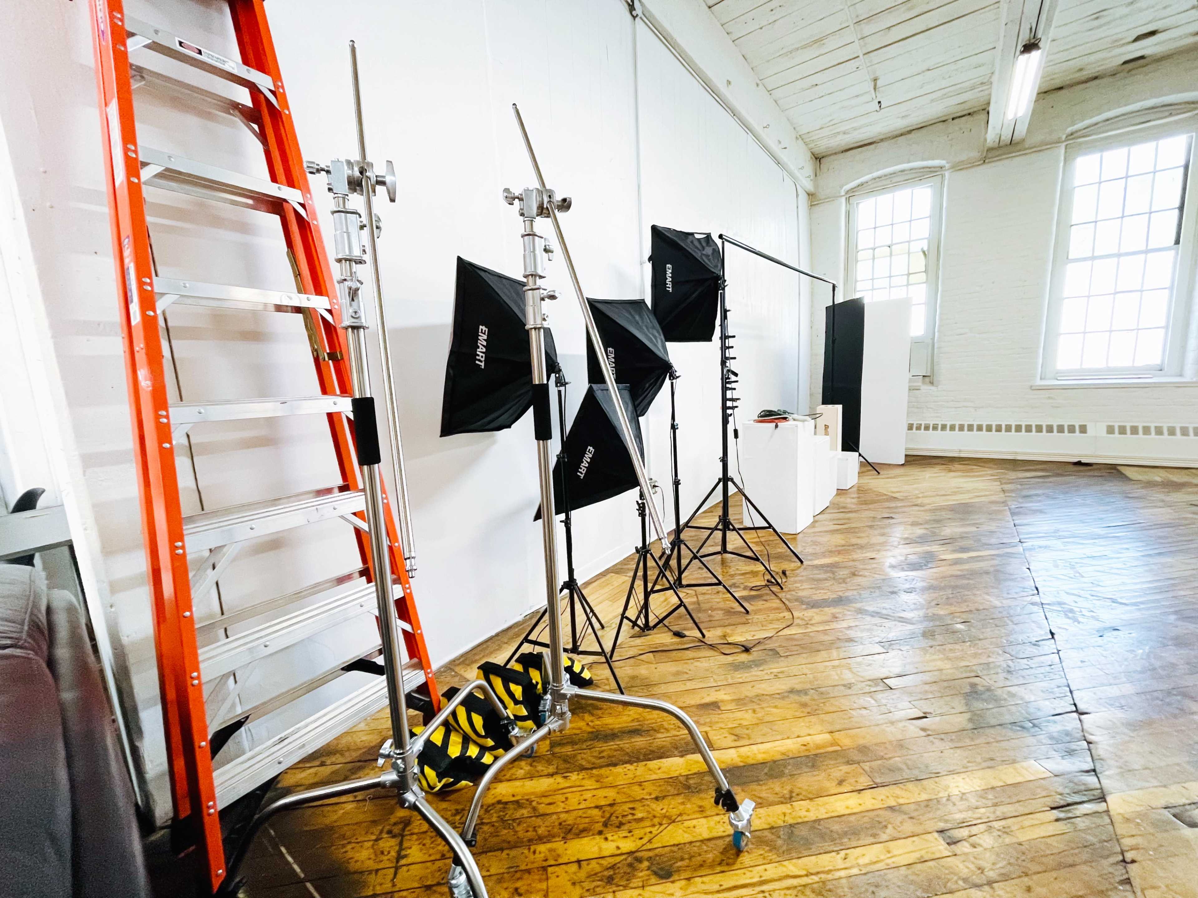 A photography studio with a wooden floor, a ladder, light stands, and lighting equipment.