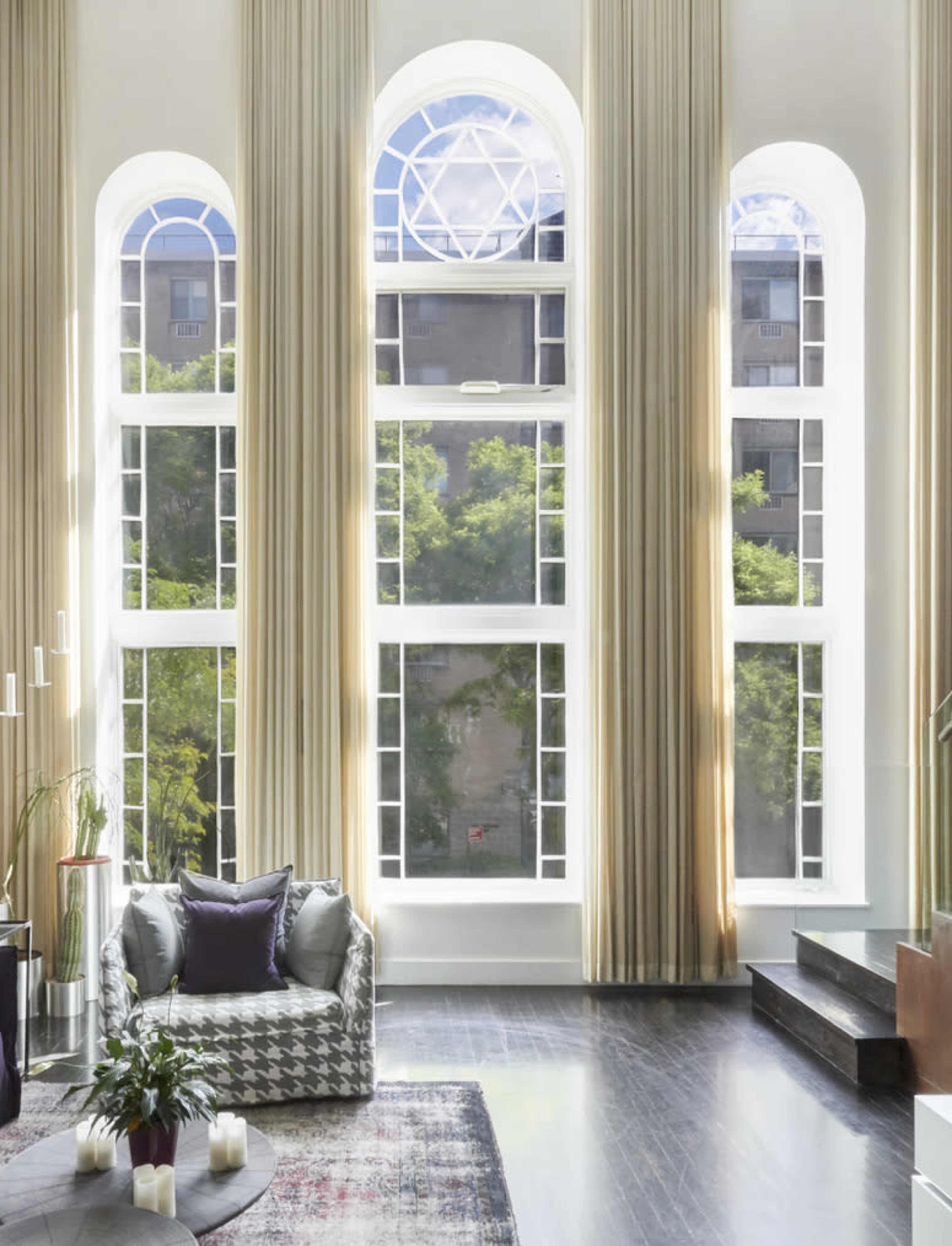 A spacious interior with large arched windows, tall drapes, and modern furniture, creating a bright atmosphere.