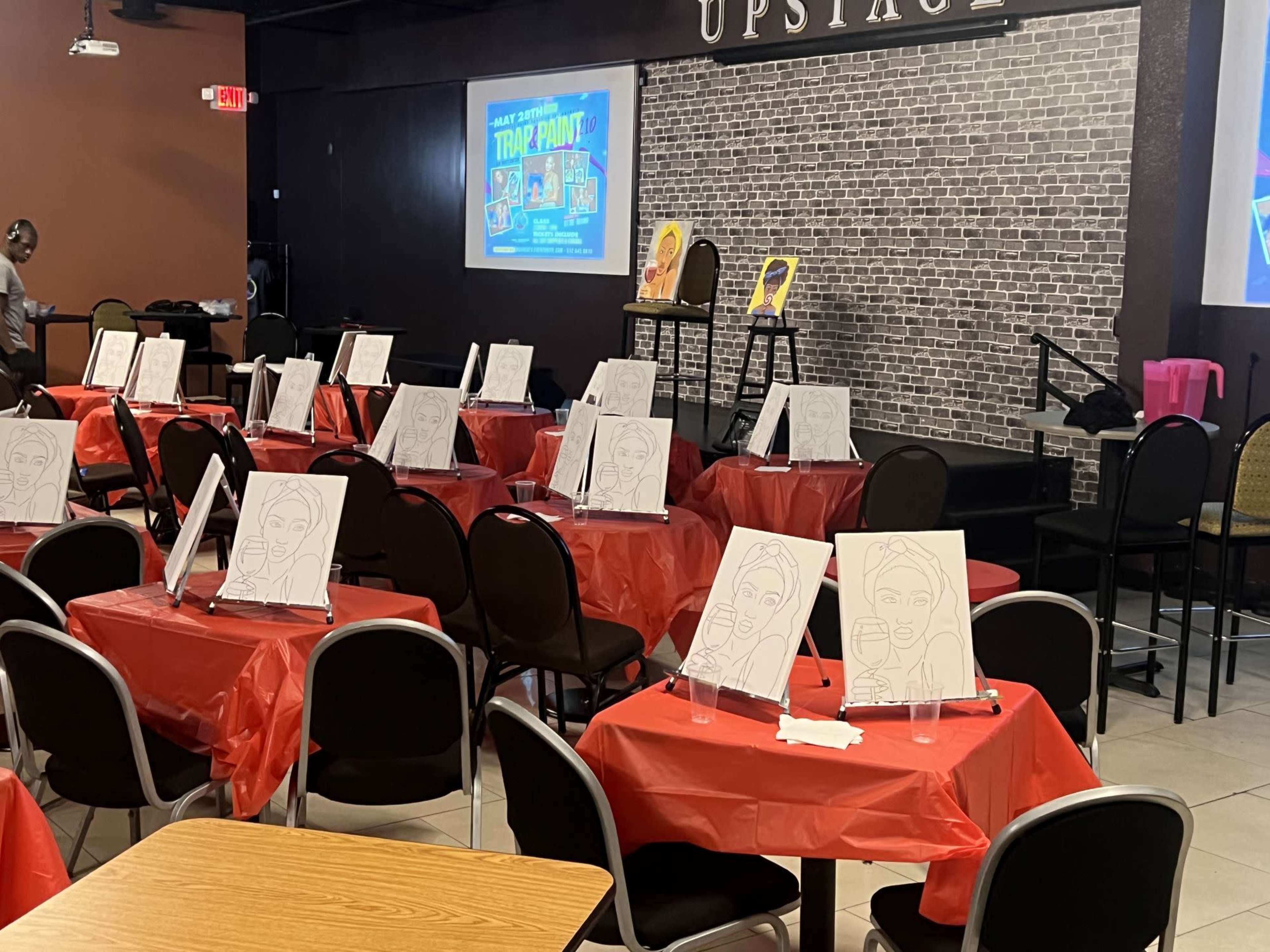 A venue set up for an art event, with tables covered in red tablecloths, each equipped with blank canvases on easels.