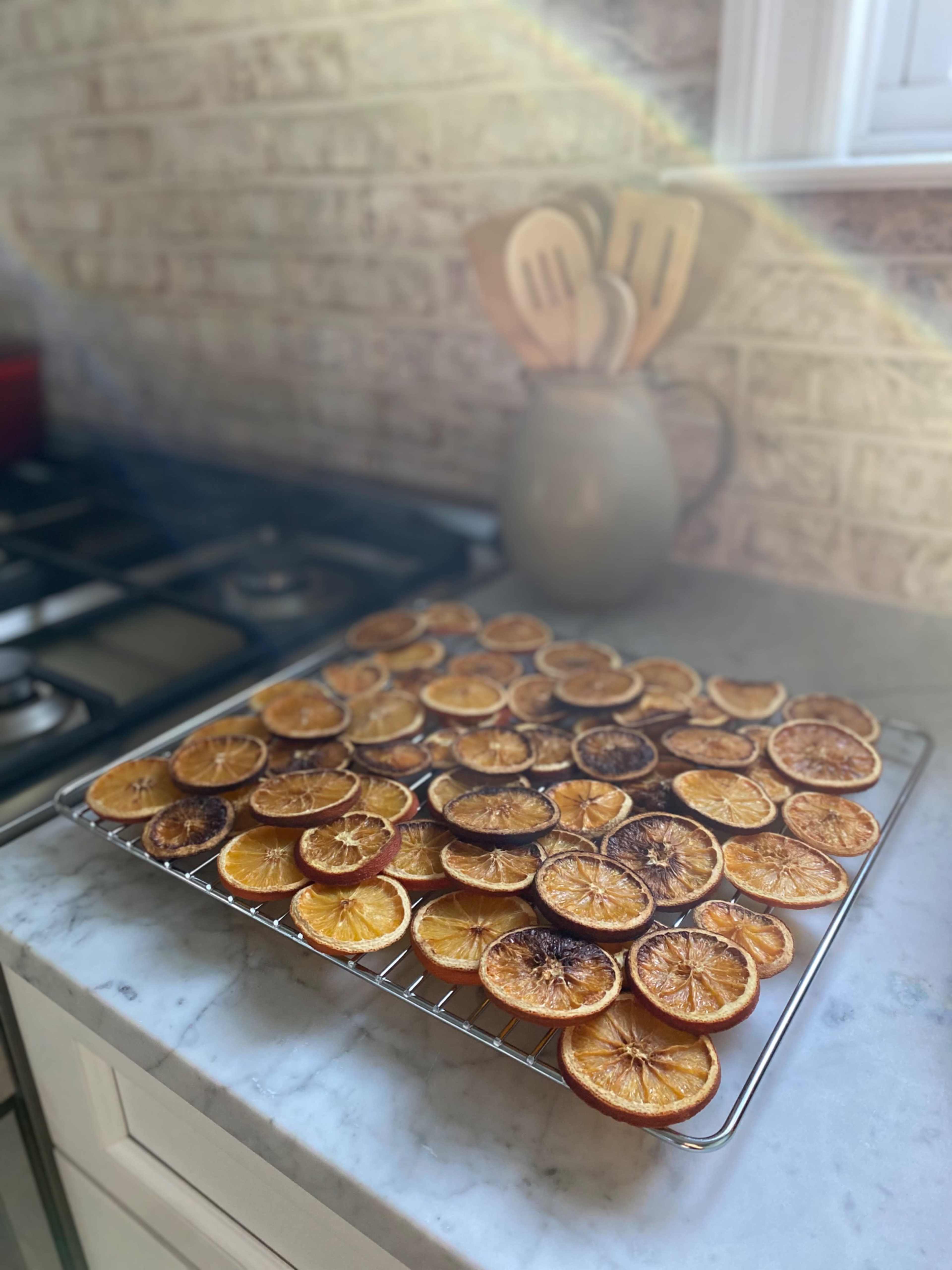 Dried orange slices are arranged on a wire rack on a marble countertop near a window.