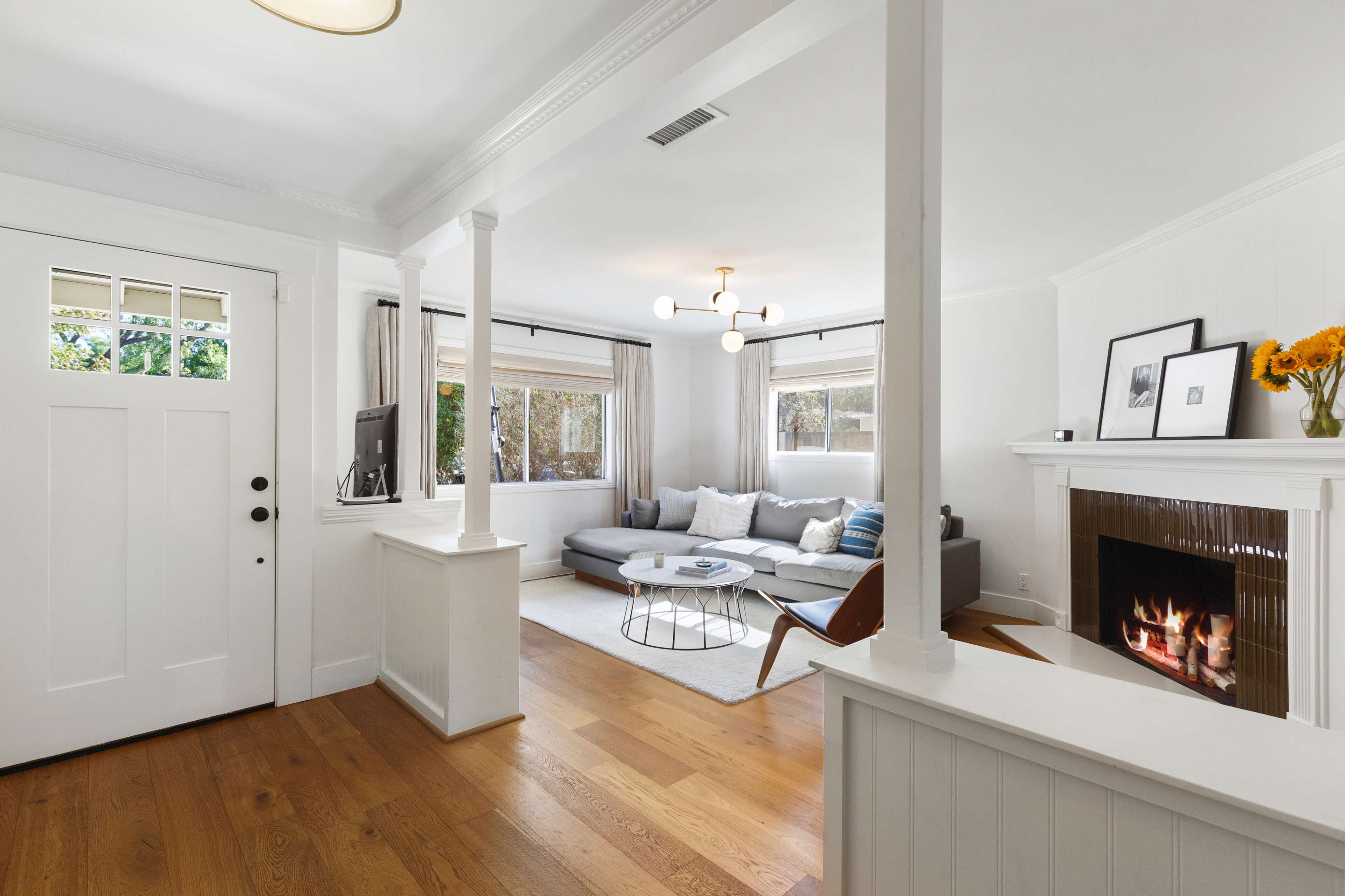 A bright living room with a gray sectional sofa, a round coffee table, and a fireplace, featuring large windows that allow natural light to enter.