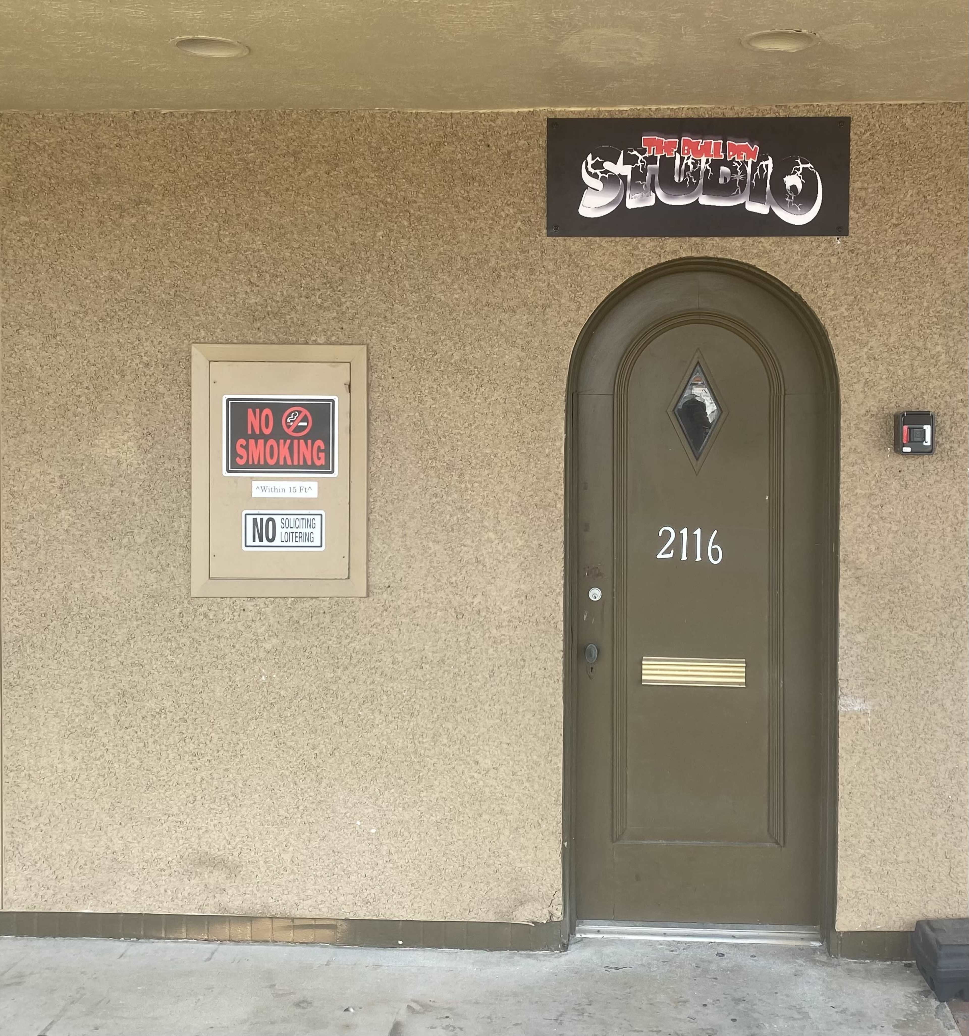 A brown door with the number 2116, situated beneath a sign that reads "The Real Boy Studio," alongside two notices indicating no smoking.