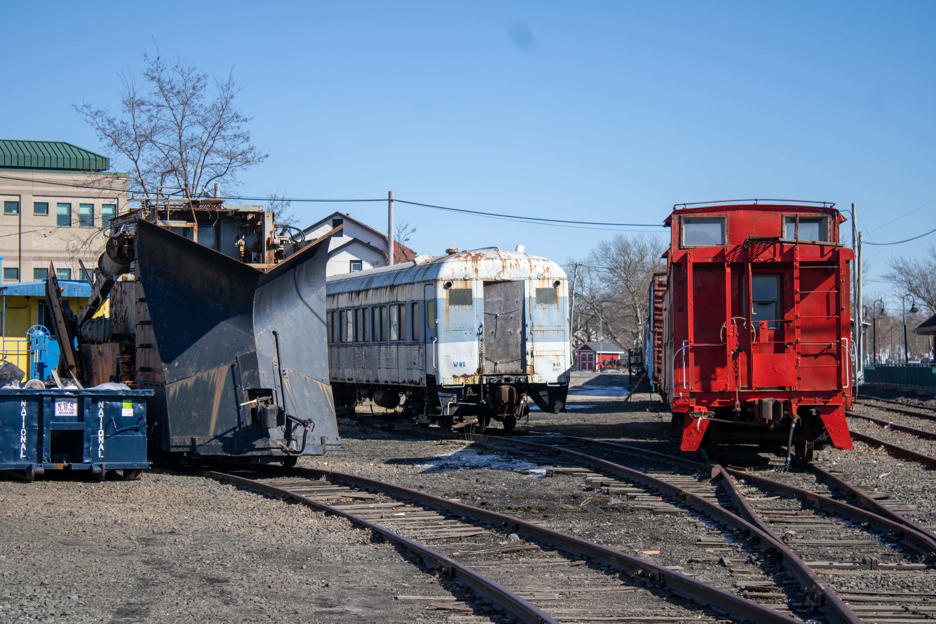 The image shows an industrial yard with a snowplow train, an old passenger car, and a red caboose on parallel tracks.