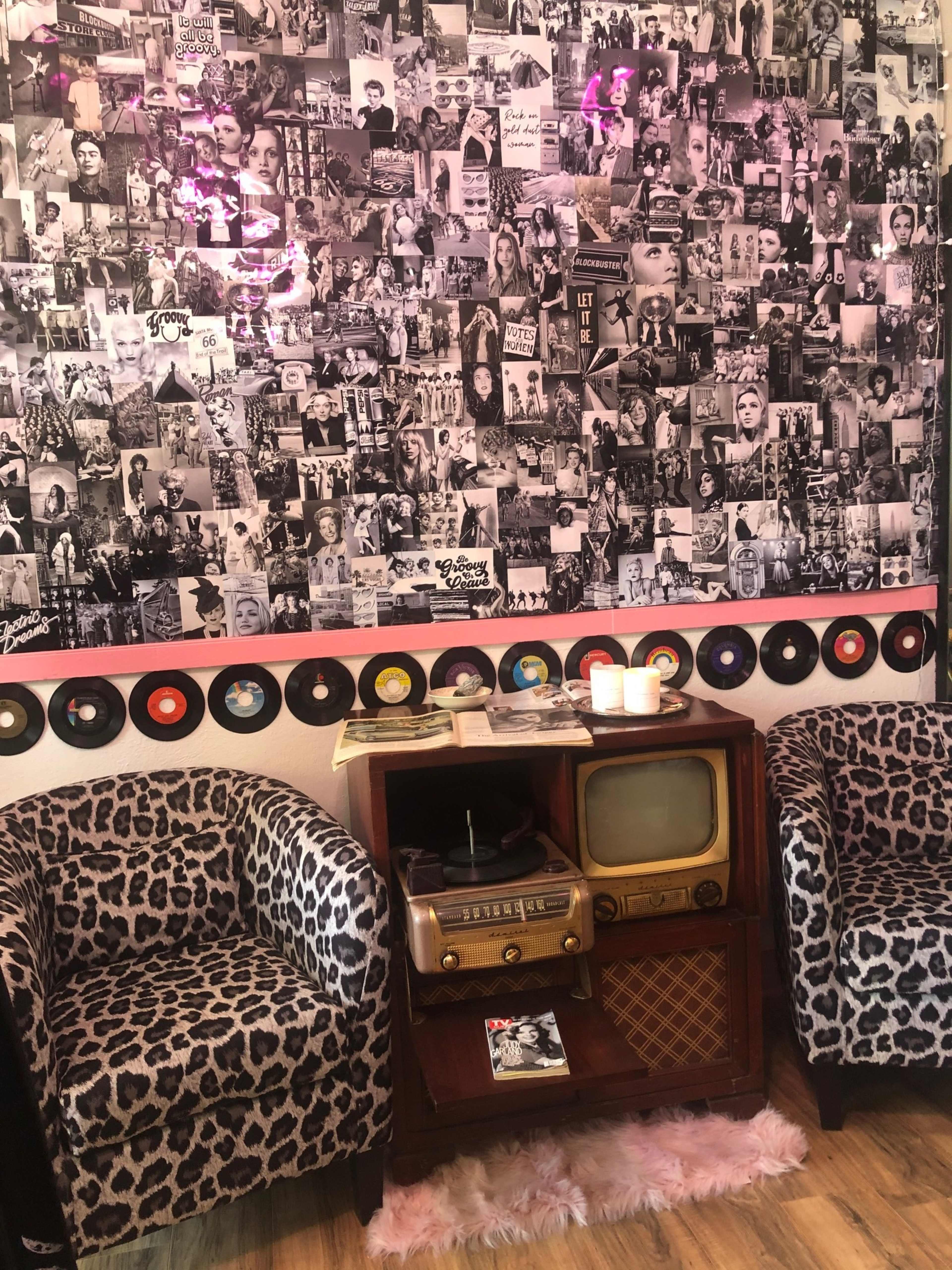 The scene features two leopard-print chairs beside a vintage radio and television set, against a wall covered with black-and-white photographs and framed records.