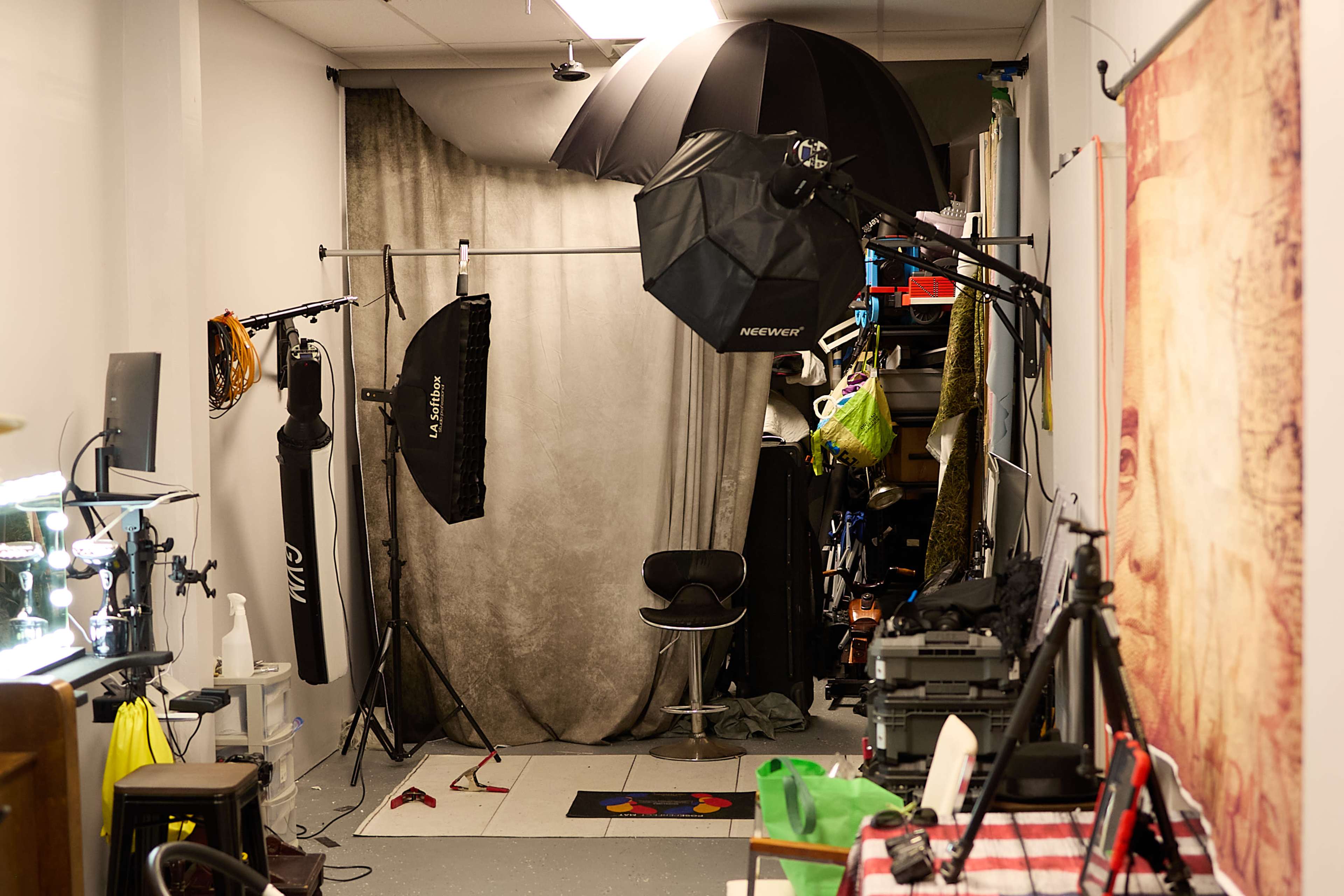 The image shows a photography studio setup with a backdrop, lighting equipment, and various props and equipment neatly stored along the walls.