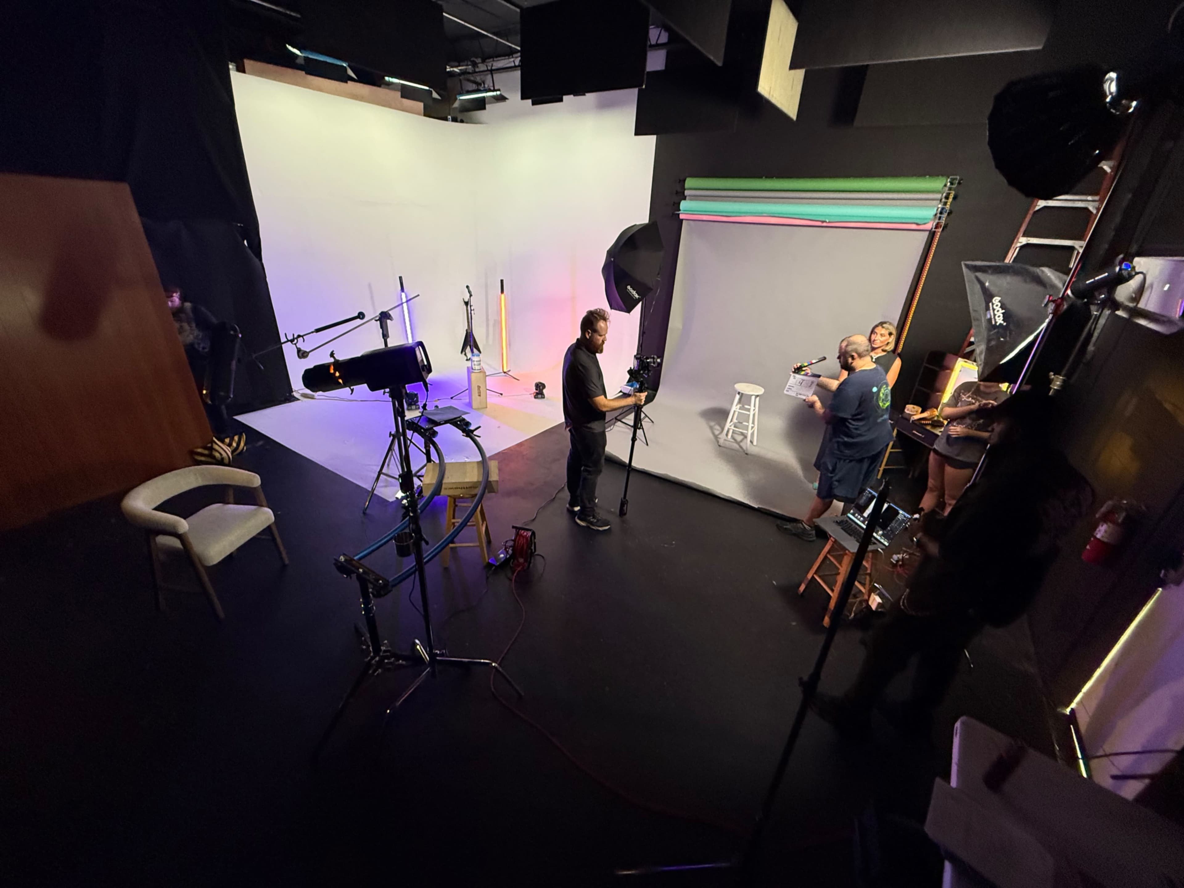 A photography studio is set up with various lighting equipment, backdrops, and camera gear, while a small group prepares for a photo shoot.