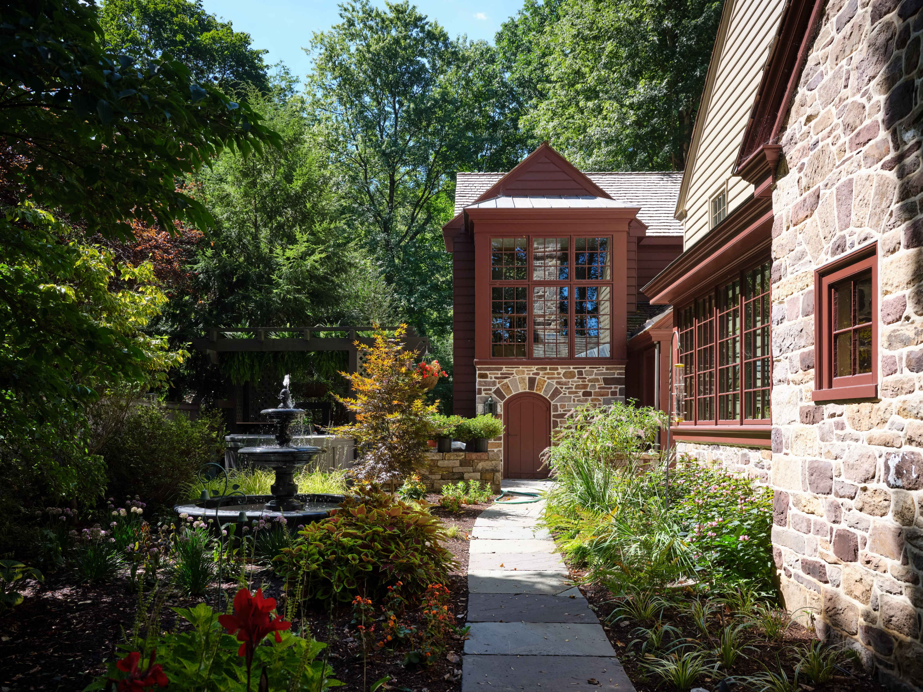 A landscaped pathway leading to a stone building with large windows, flanked by greenery and a fountain.