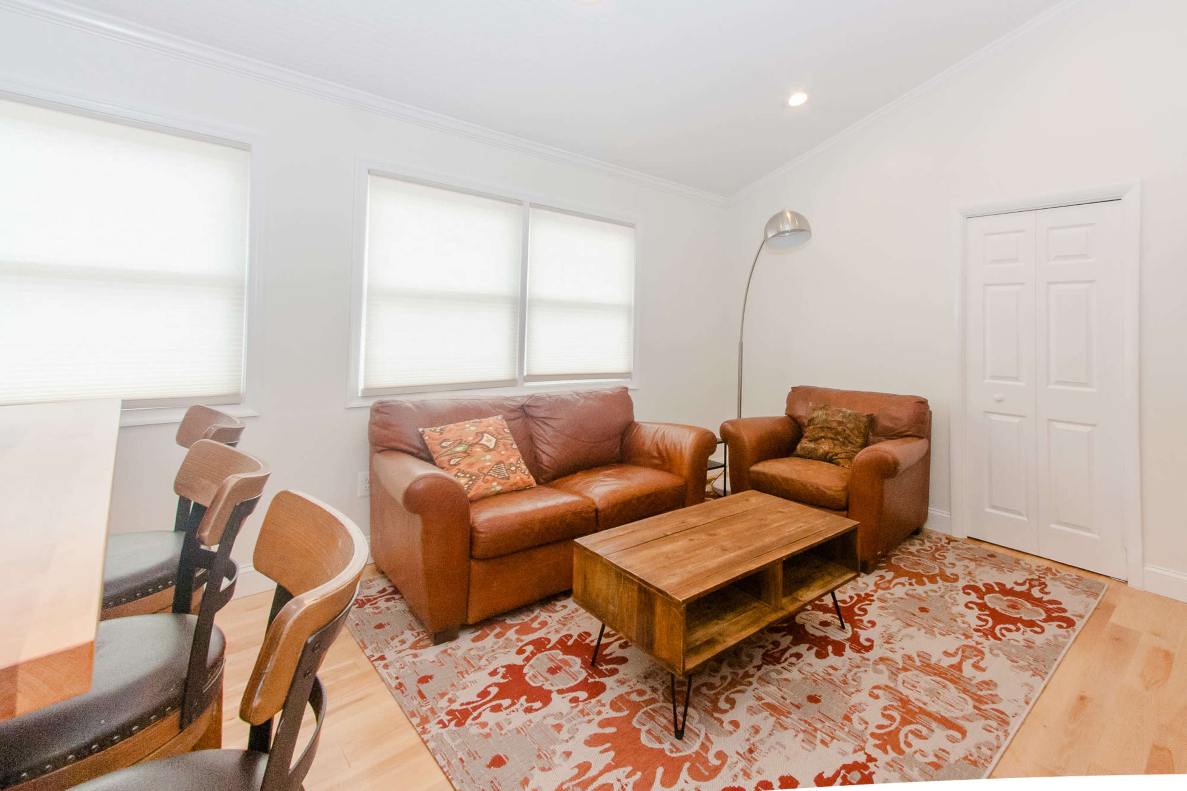 A living room with two brown leather sofas, a wooden coffee table, and a chair, set against a backdrop of light walls and large windows.