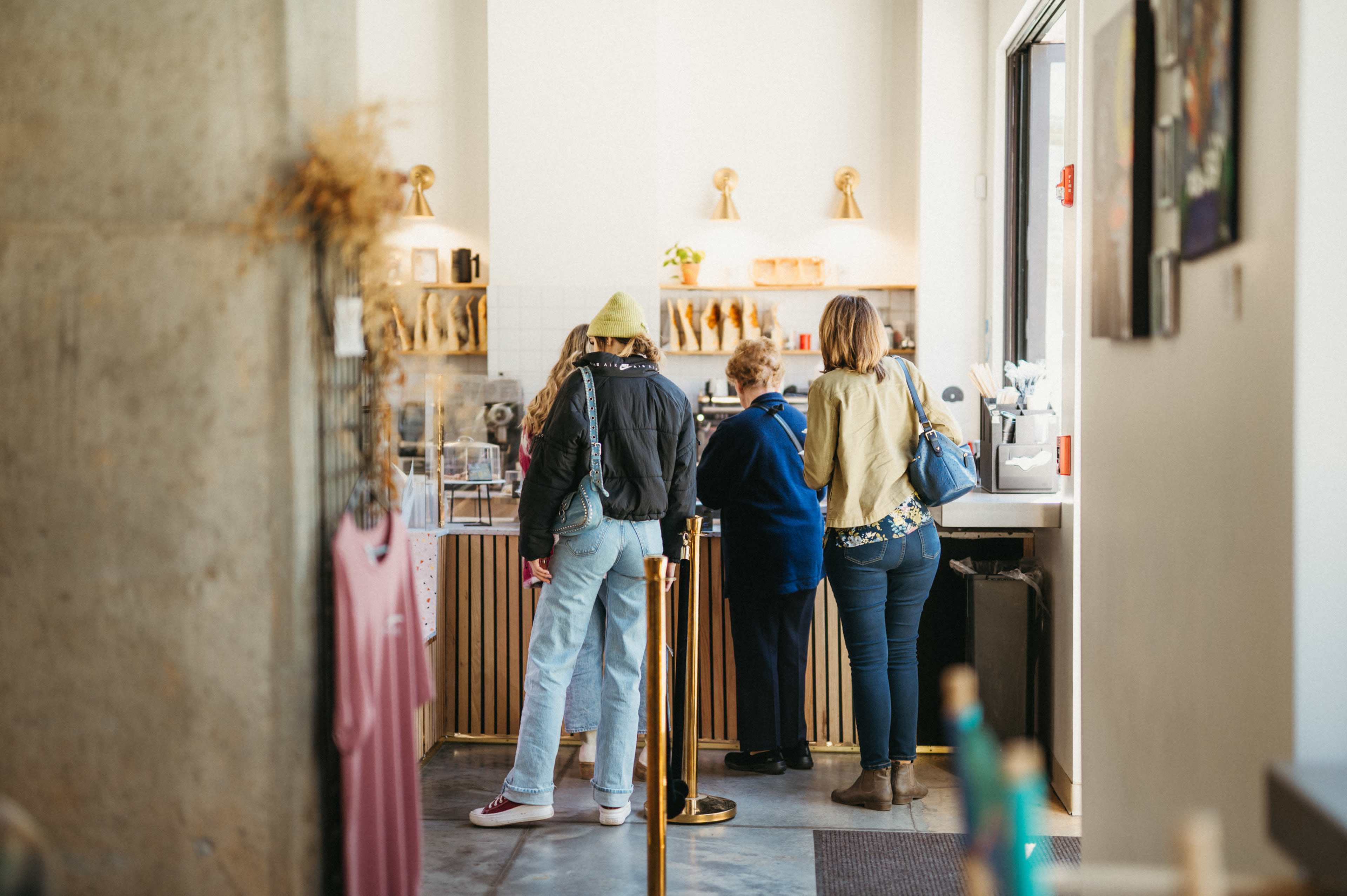 A group of three people stands in line at a counter inside a café.