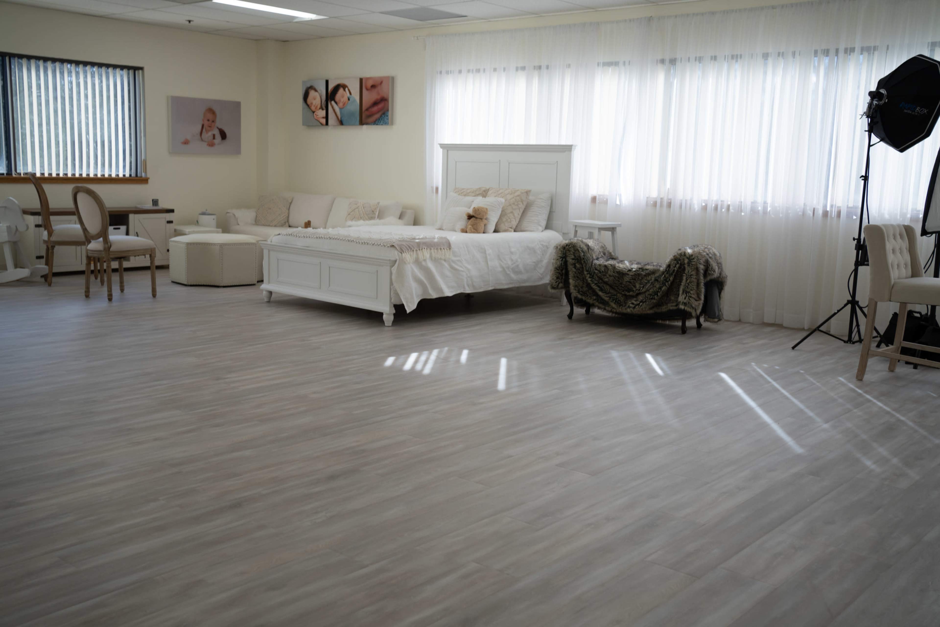 A bright, spacious room with light-colored flooring, a large bed, and comfortable seating arranged near windows with sheer curtains.