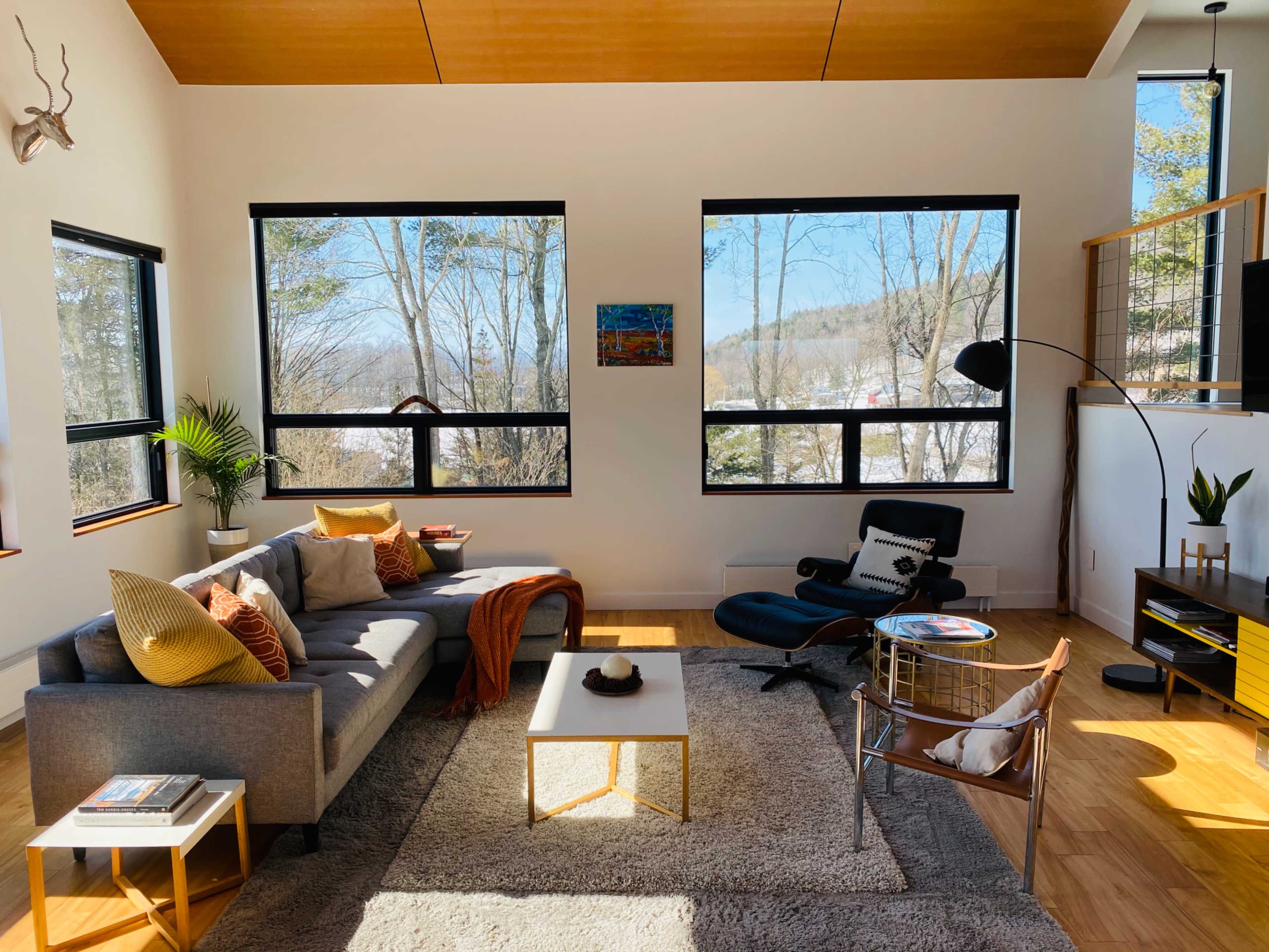 A modern living room featuring a gray sectional sofa, a coffee table, and large windows overlooking a forested area.