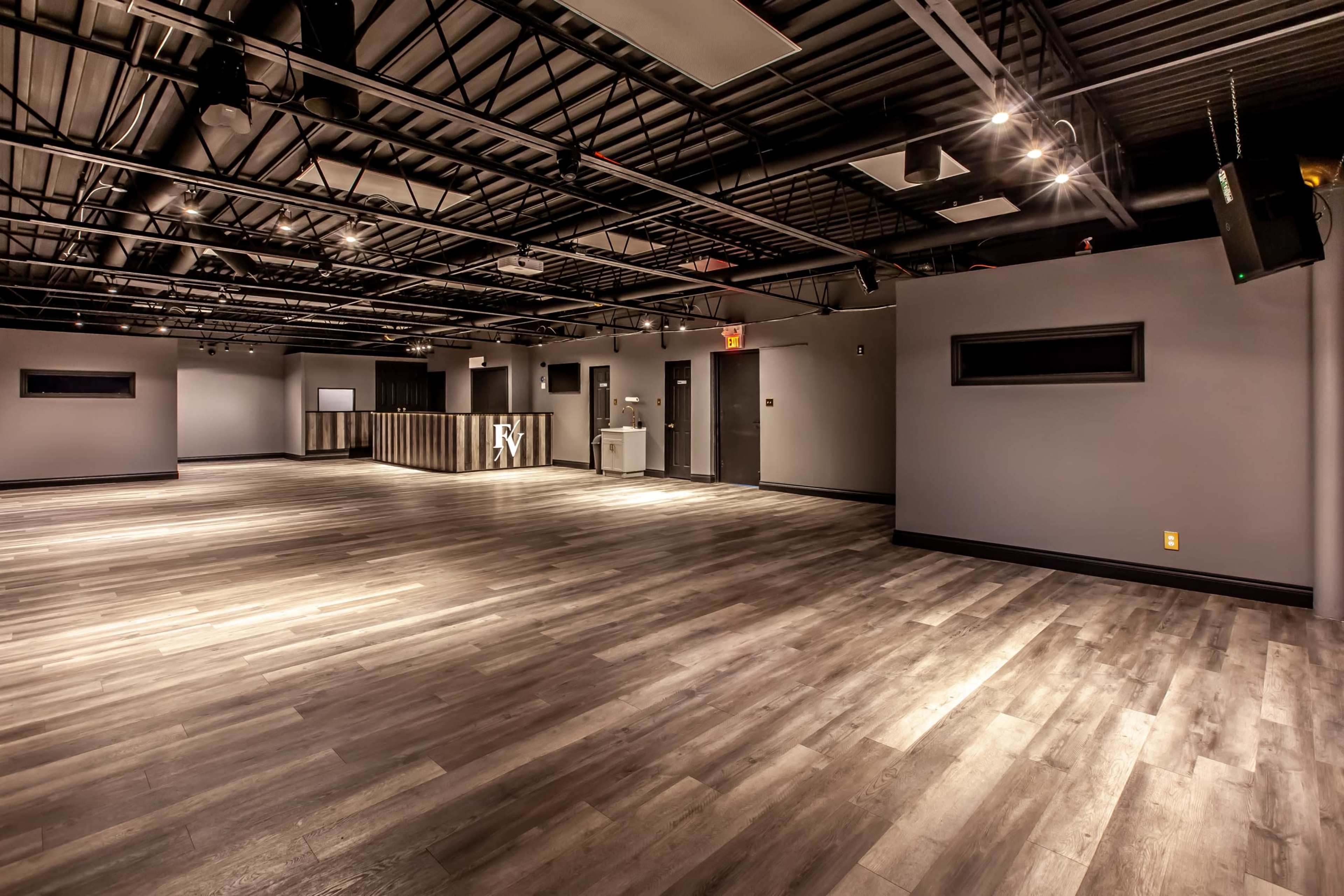 An empty, modern interior space with wooden flooring and a ceiling supported by exposed beams and lighting fixtures.