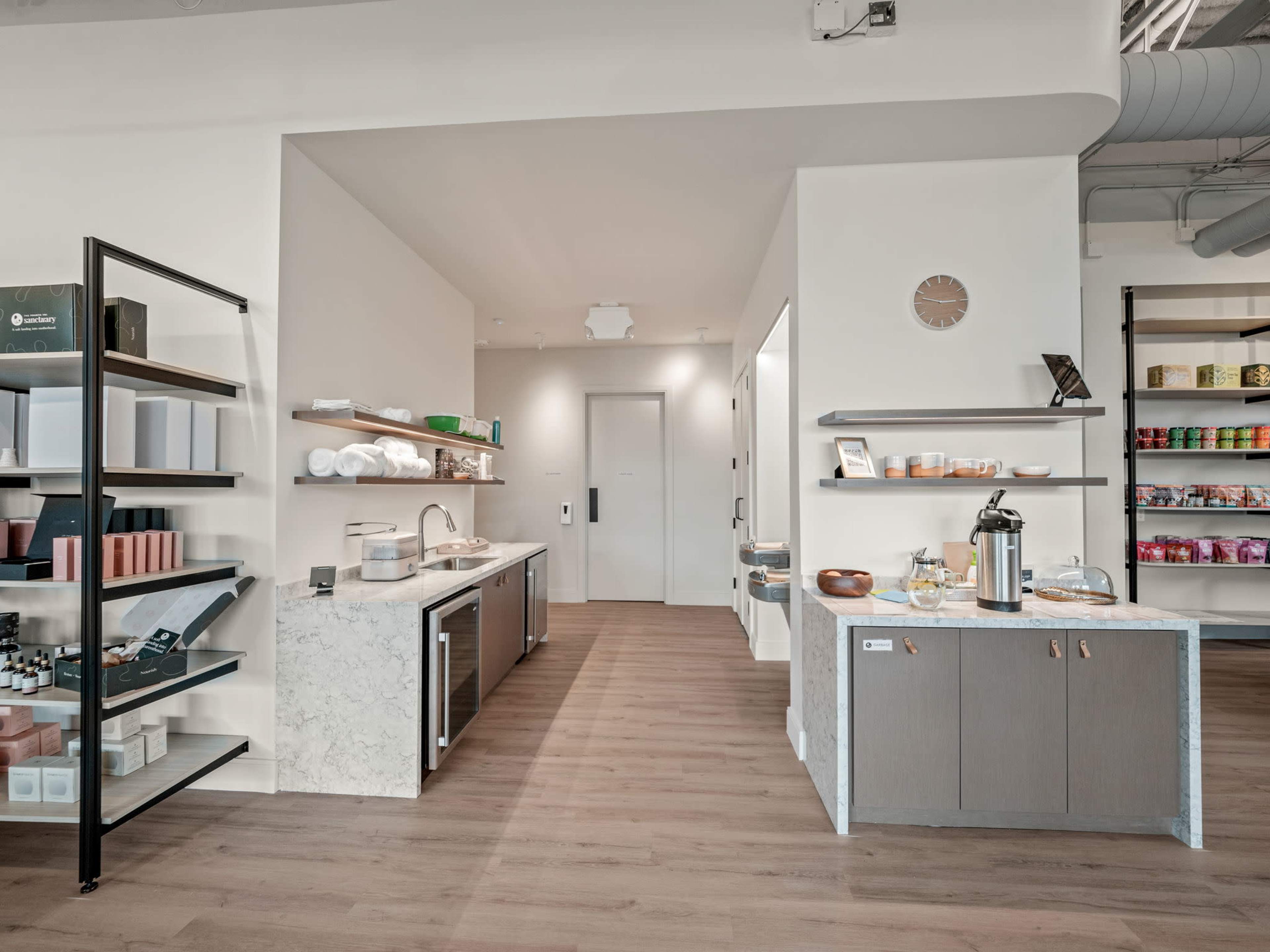 A modern interior features a kitchen area with a marble countertop and organized shelves displaying storage containers and products.