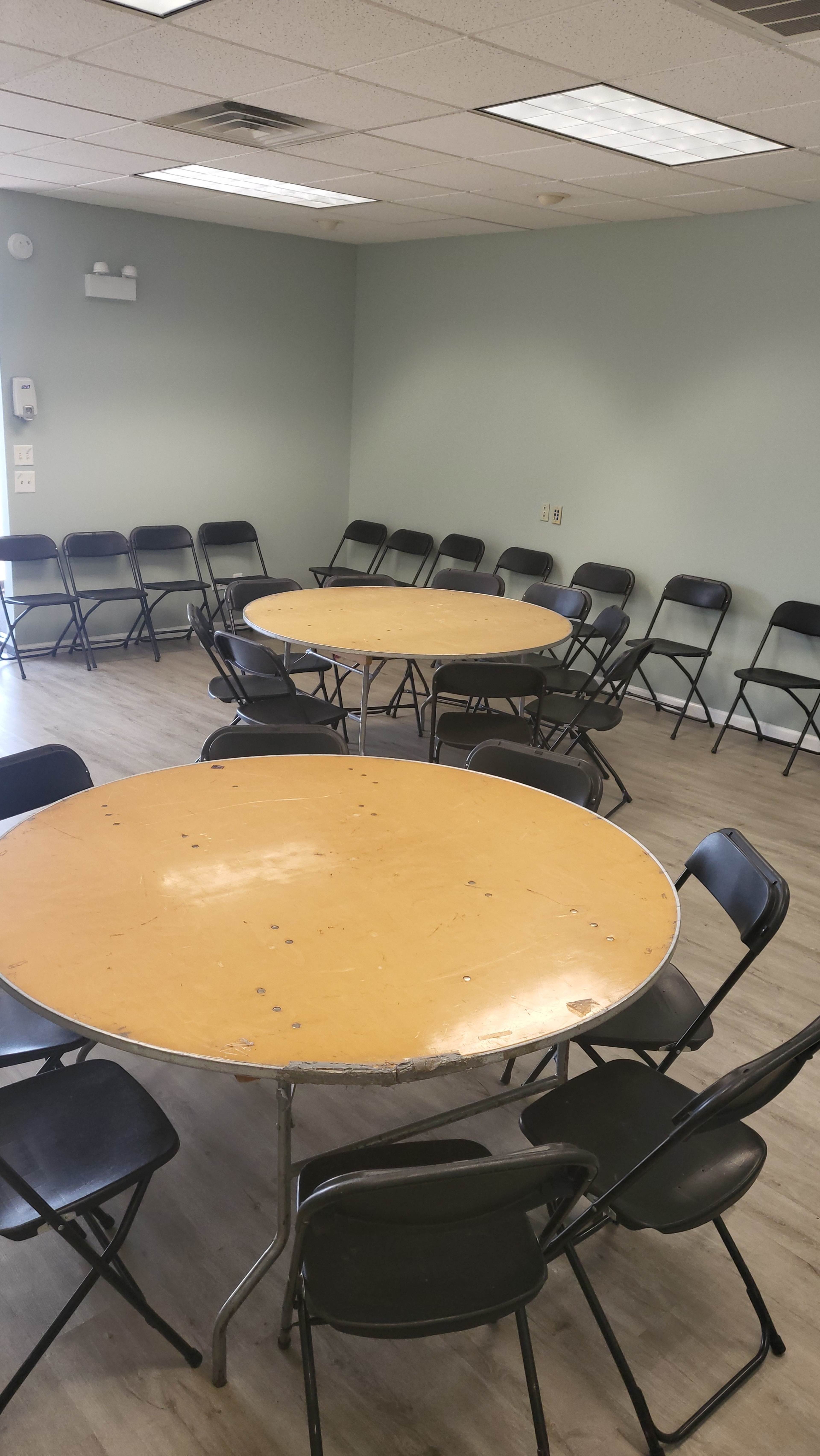 A meeting room with two round tables surrounded by black folding chairs arranged in a circle on a wooden floor.