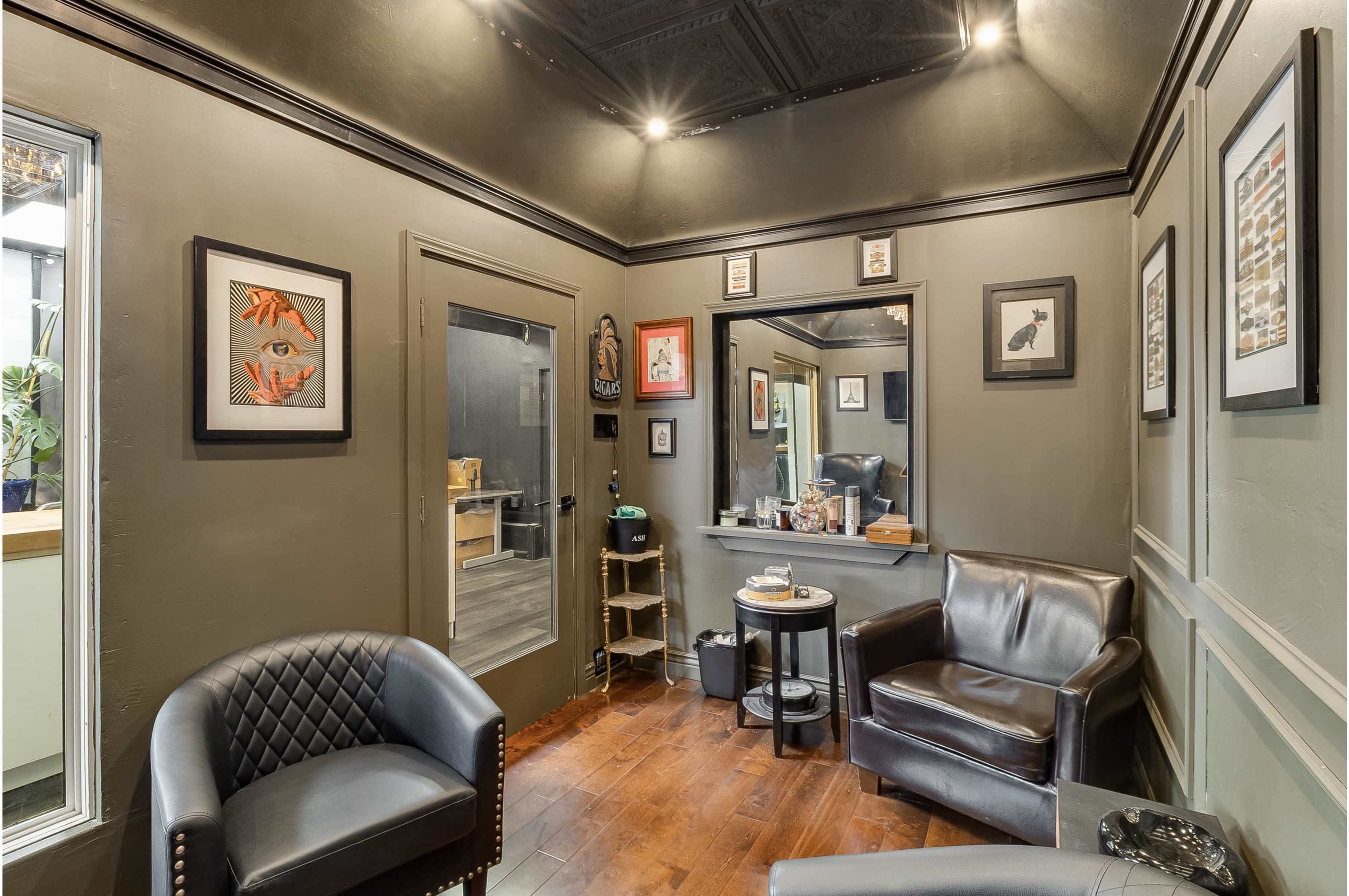 The image shows a small, dimly lit sitting area with dark walls, framed artwork, and leather furniture.