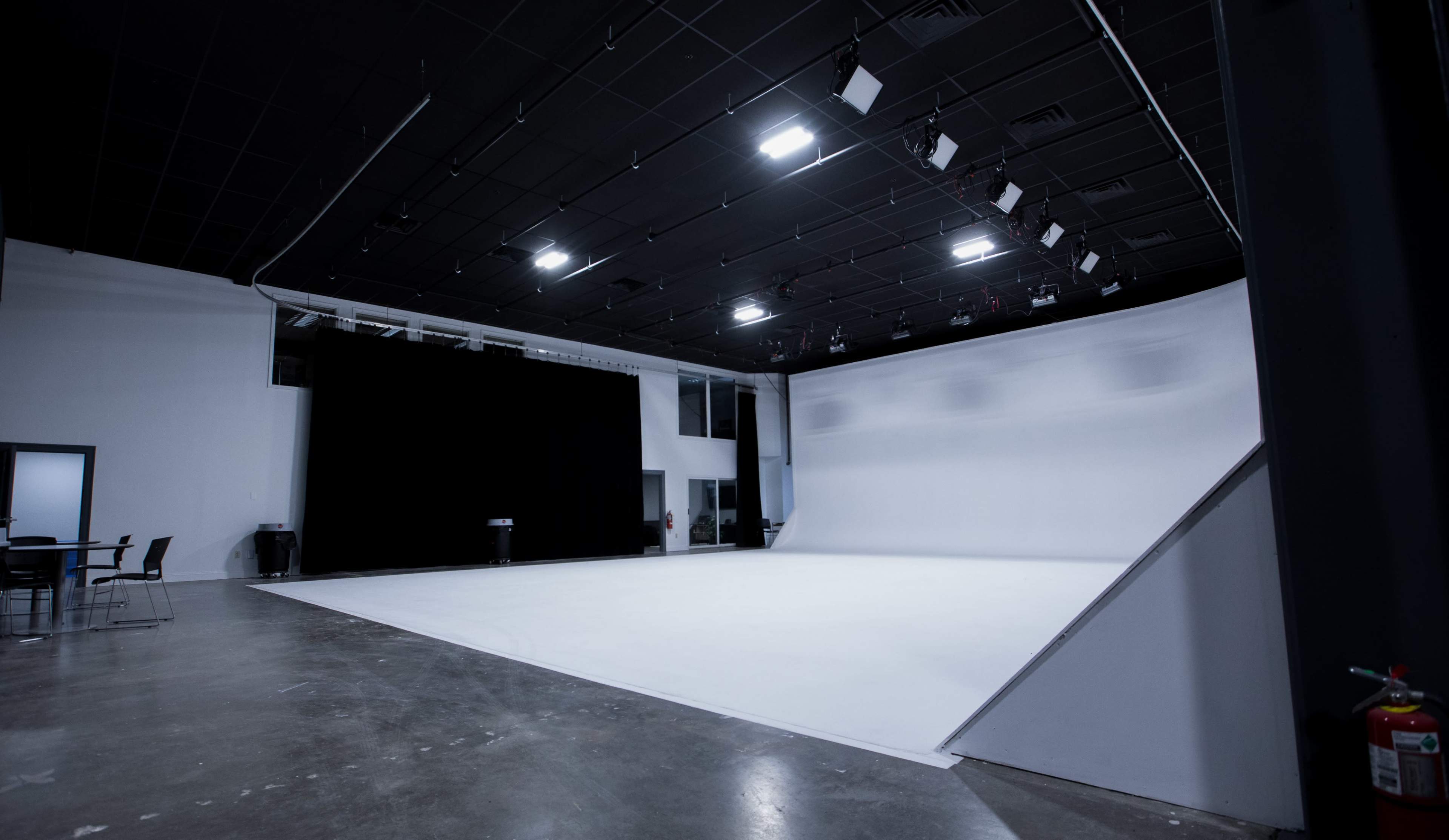 The image shows a spacious photography studio with a large, white backdrop and overhead lighting.