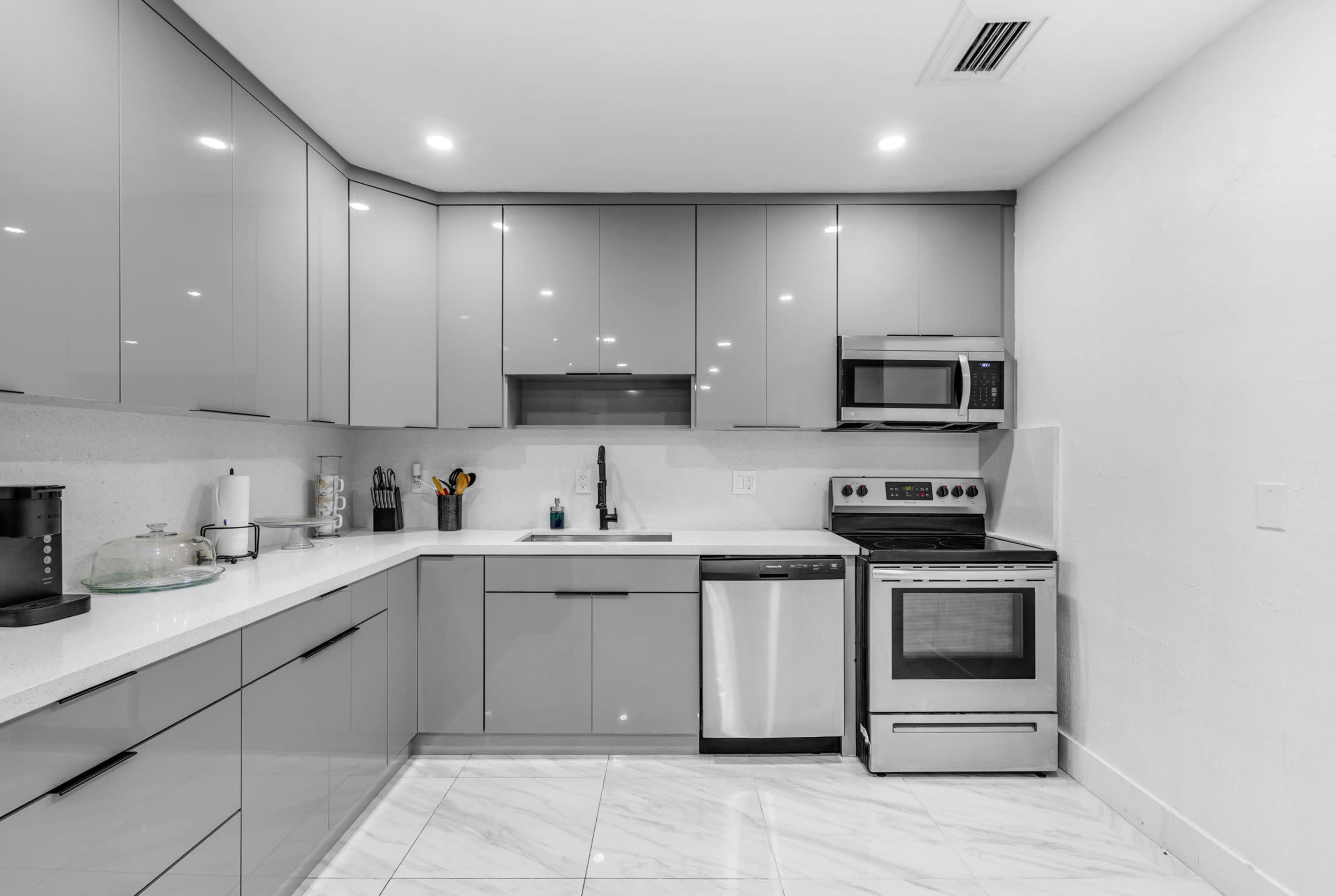 The image shows a modern kitchen fitted with sleek gray cabinets, stainless steel appliances, and white countertops.