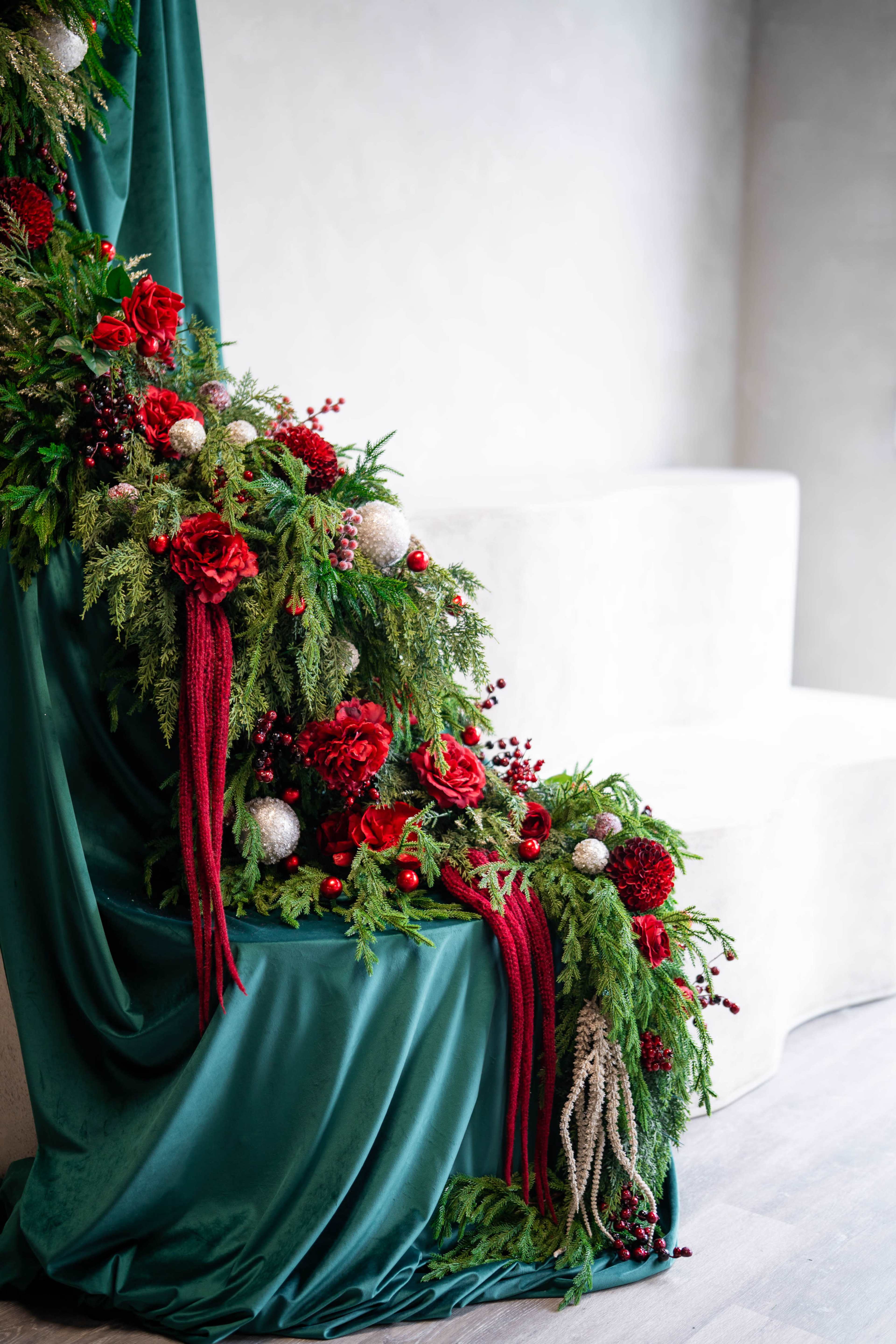 The image features a decorative arrangement of red flowers, greenery, and ornaments draped over a teal fabric background, setting a festive scene.