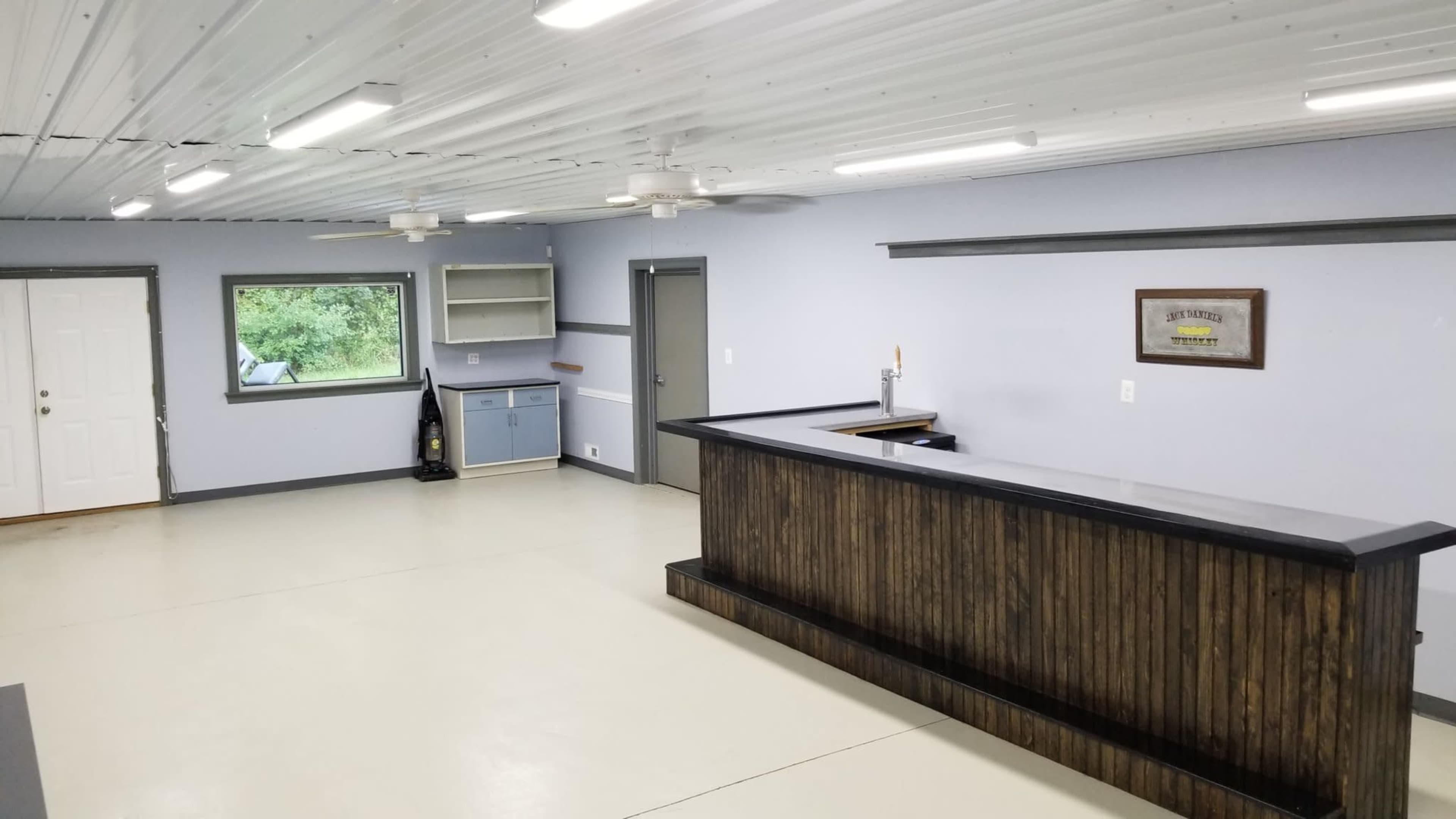 An empty room with a counter, a door, a window, and a kitchen area along one wall.