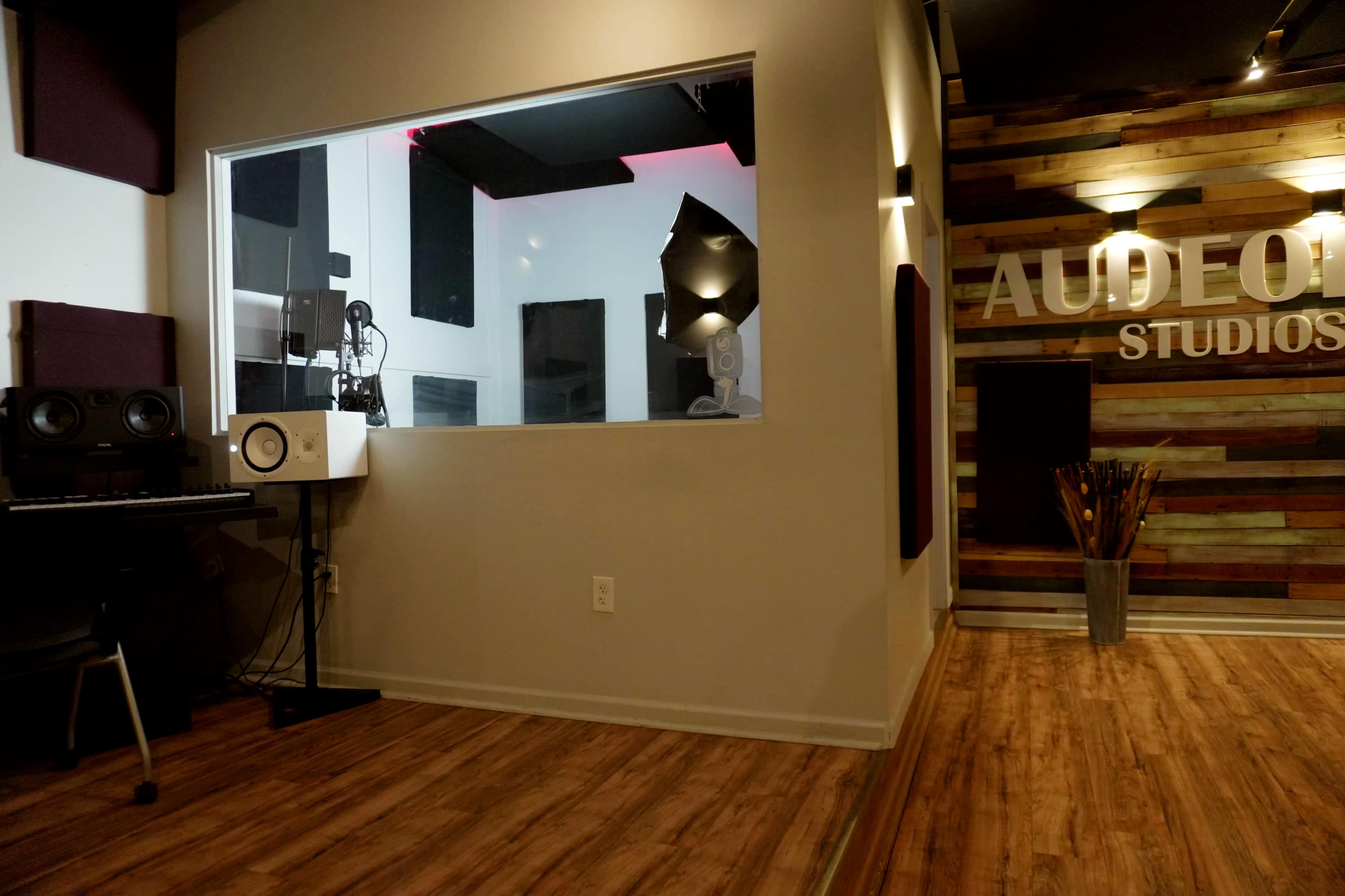 A recording studio interior with a large window separating the control room from the tracking area, featuring wooden walls and a modern design.