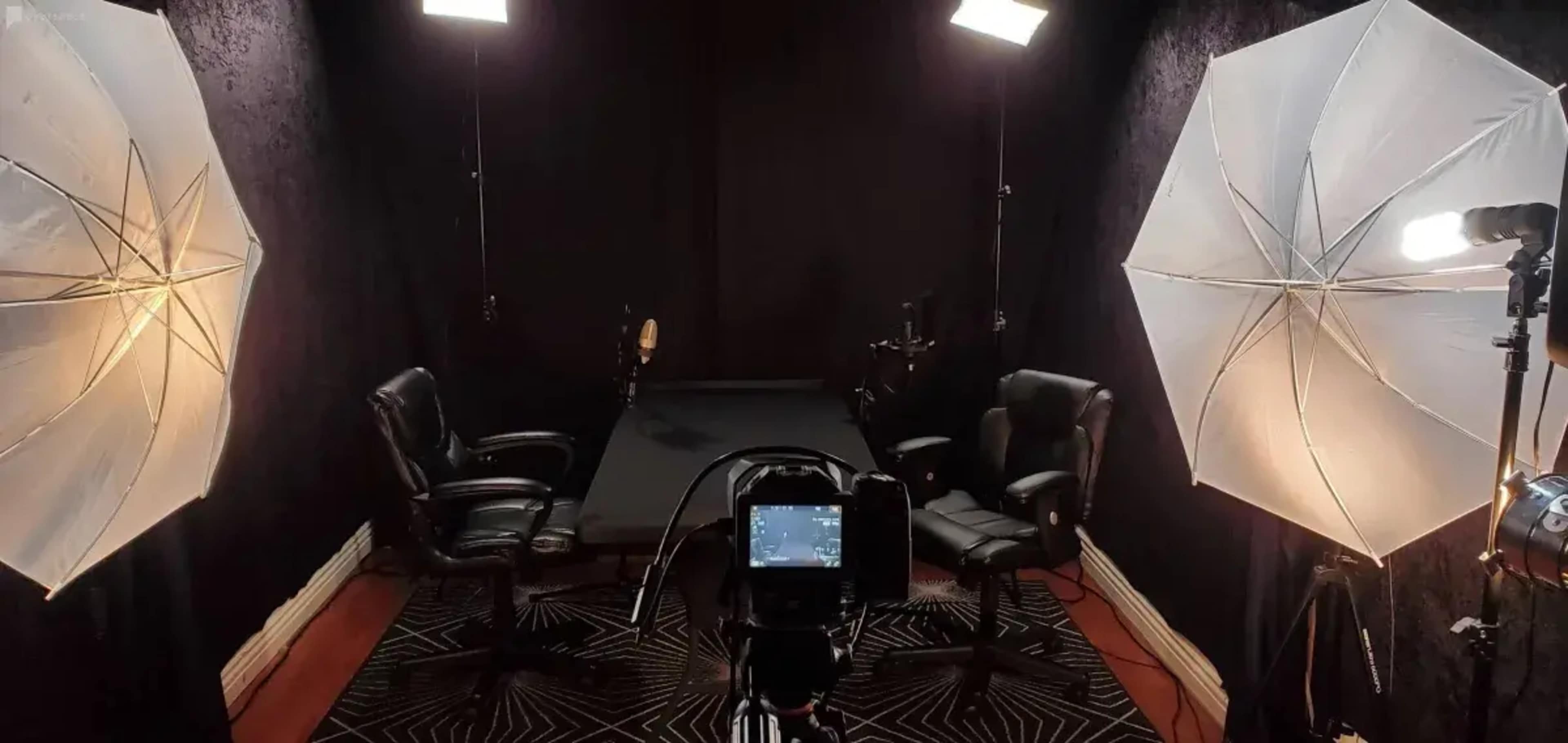 The image shows a photography studio setup with two chairs, a central table, and lighting equipment arranged on either side.