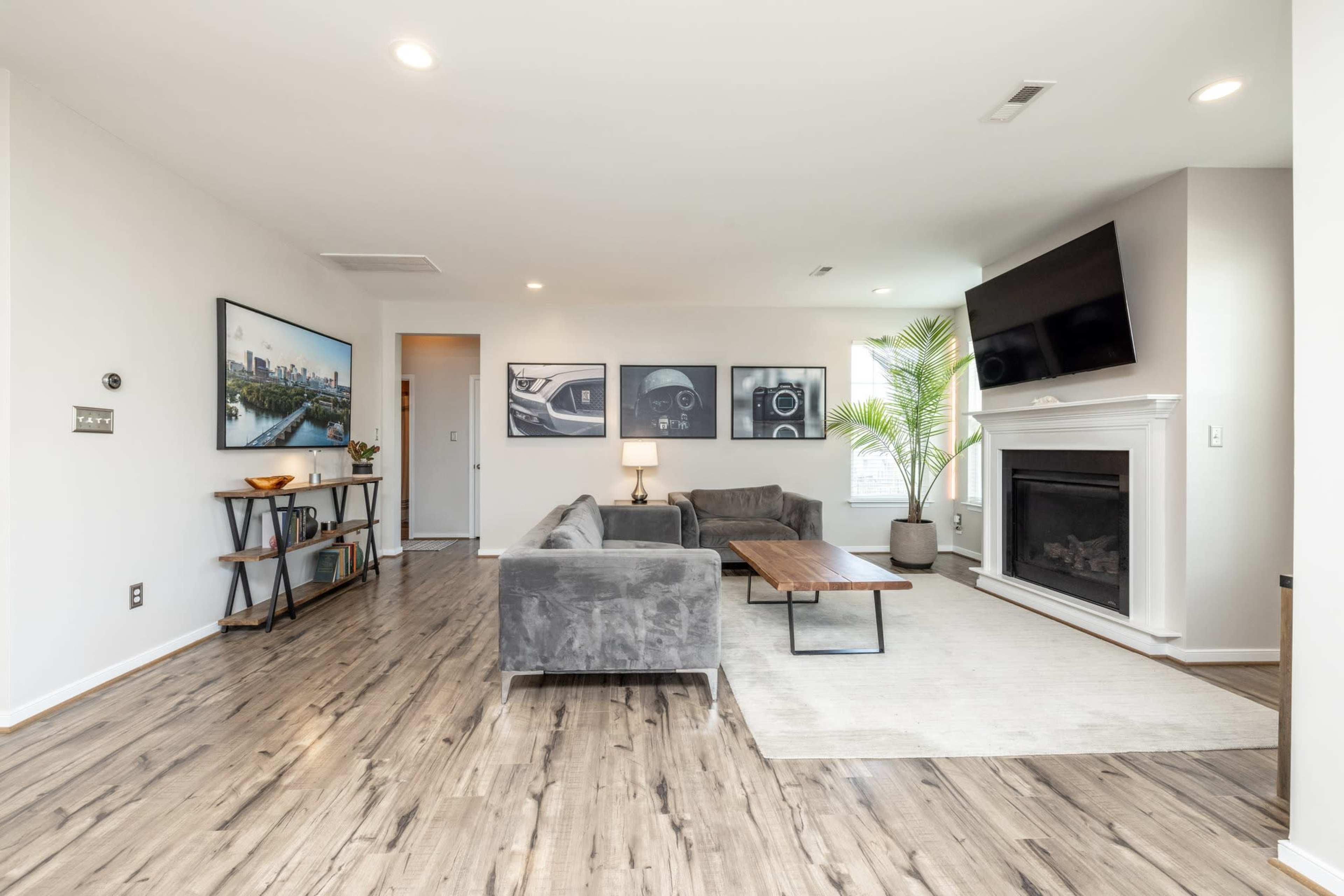 The image shows a modern living room with a gray sectional sofa, a coffee table, a fireplace, and artwork on the walls.