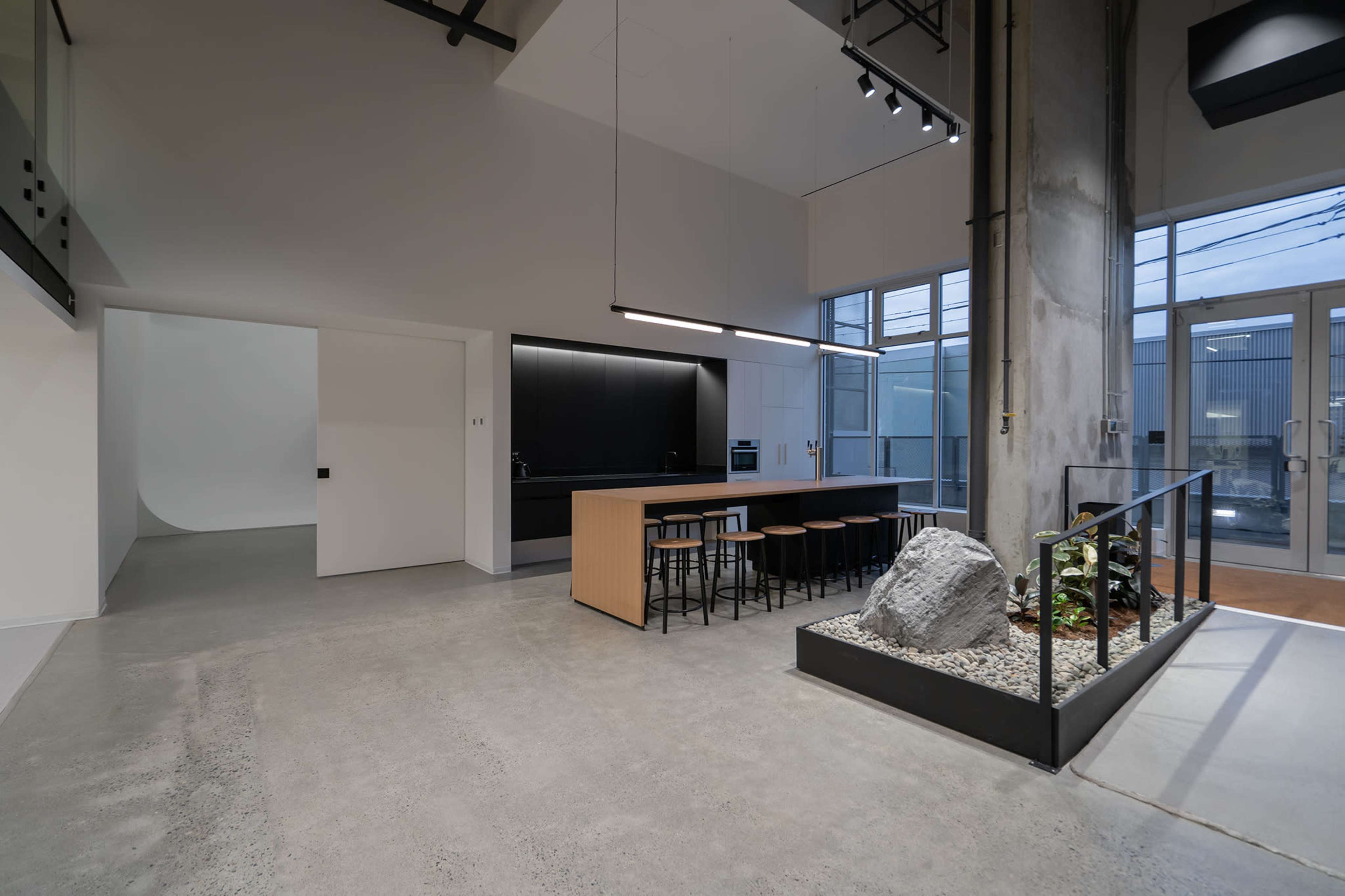 A modern, open interior space featuring a kitchen island with bar stools, concrete flooring, and large windows that allow natural light.