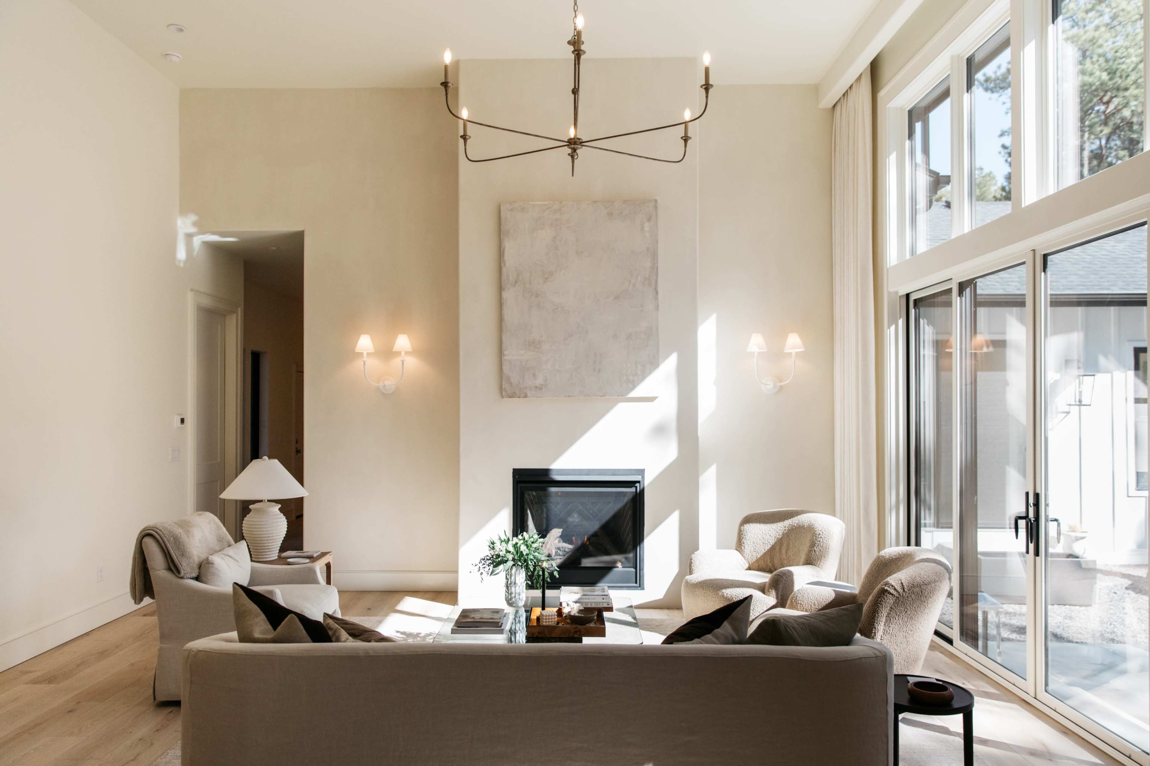 A modern living room with a fireplace, two armchairs, a sofa, and large windows that allow natural light to fill the space.