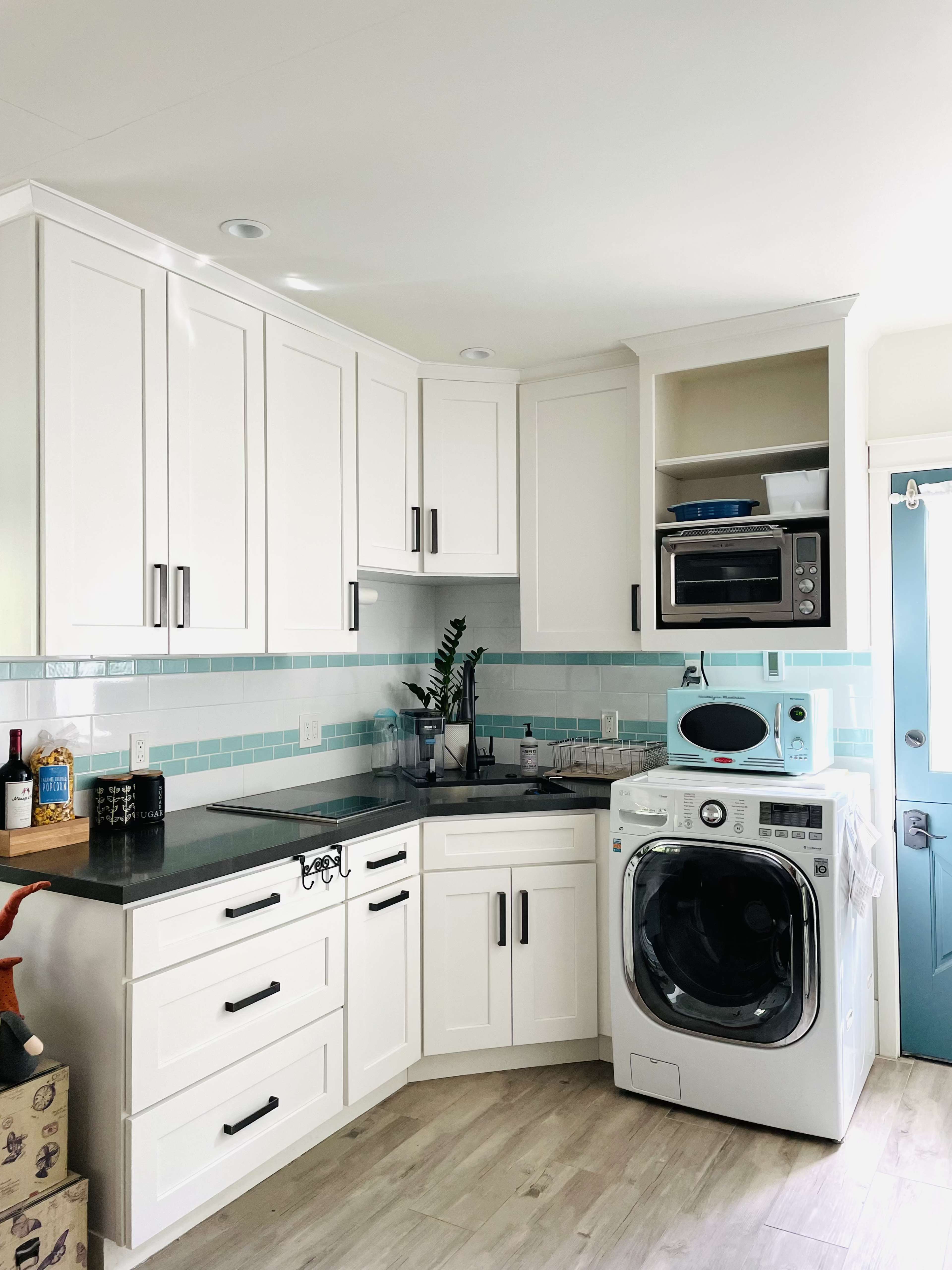 The image shows a modern kitchen with white cabinetry, a built-in microwave, and a washing machine integrated into the design.