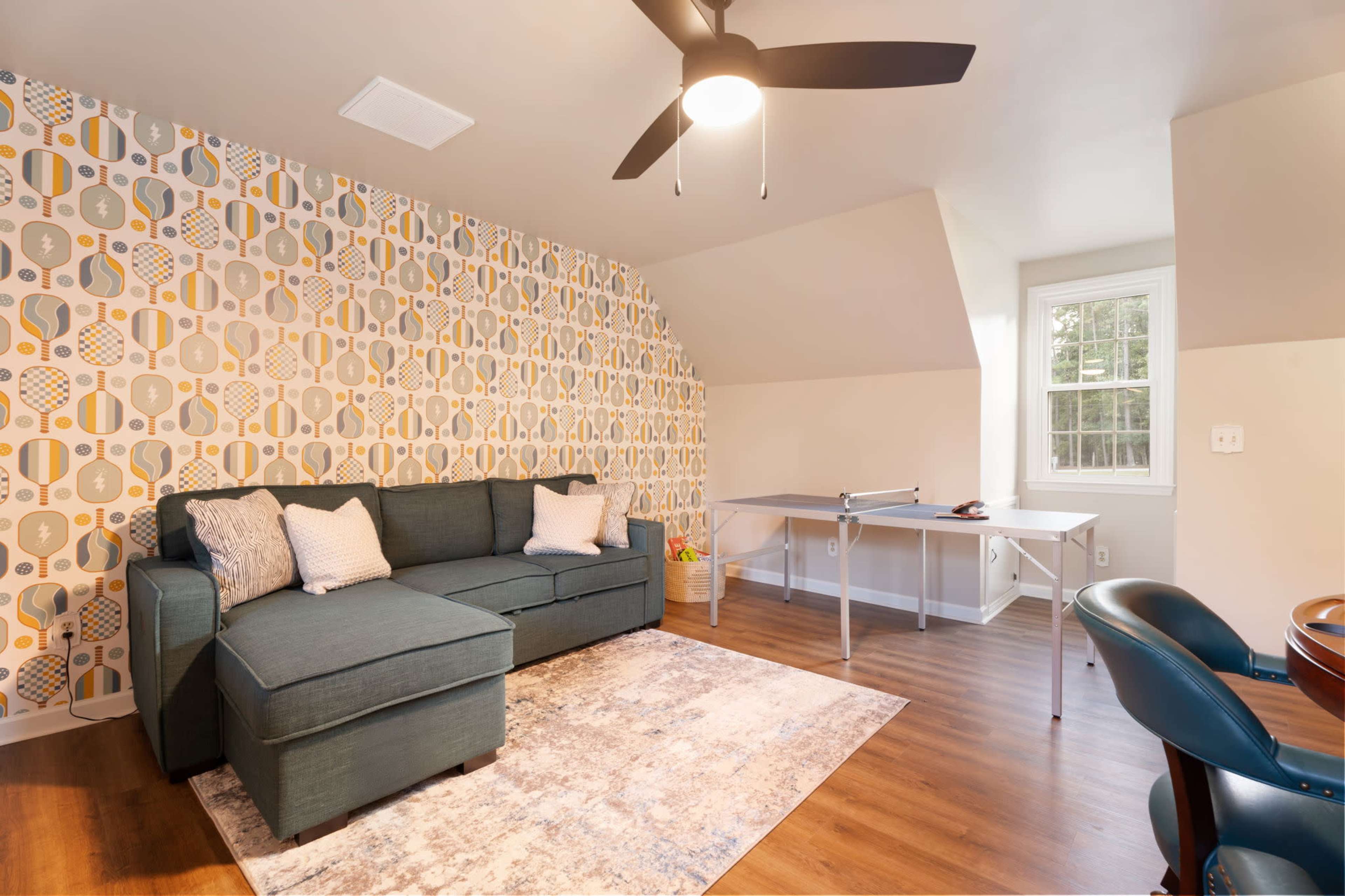 The image shows a cozy living space featuring a sectional sofa, a small table, and a patterned accent wall.