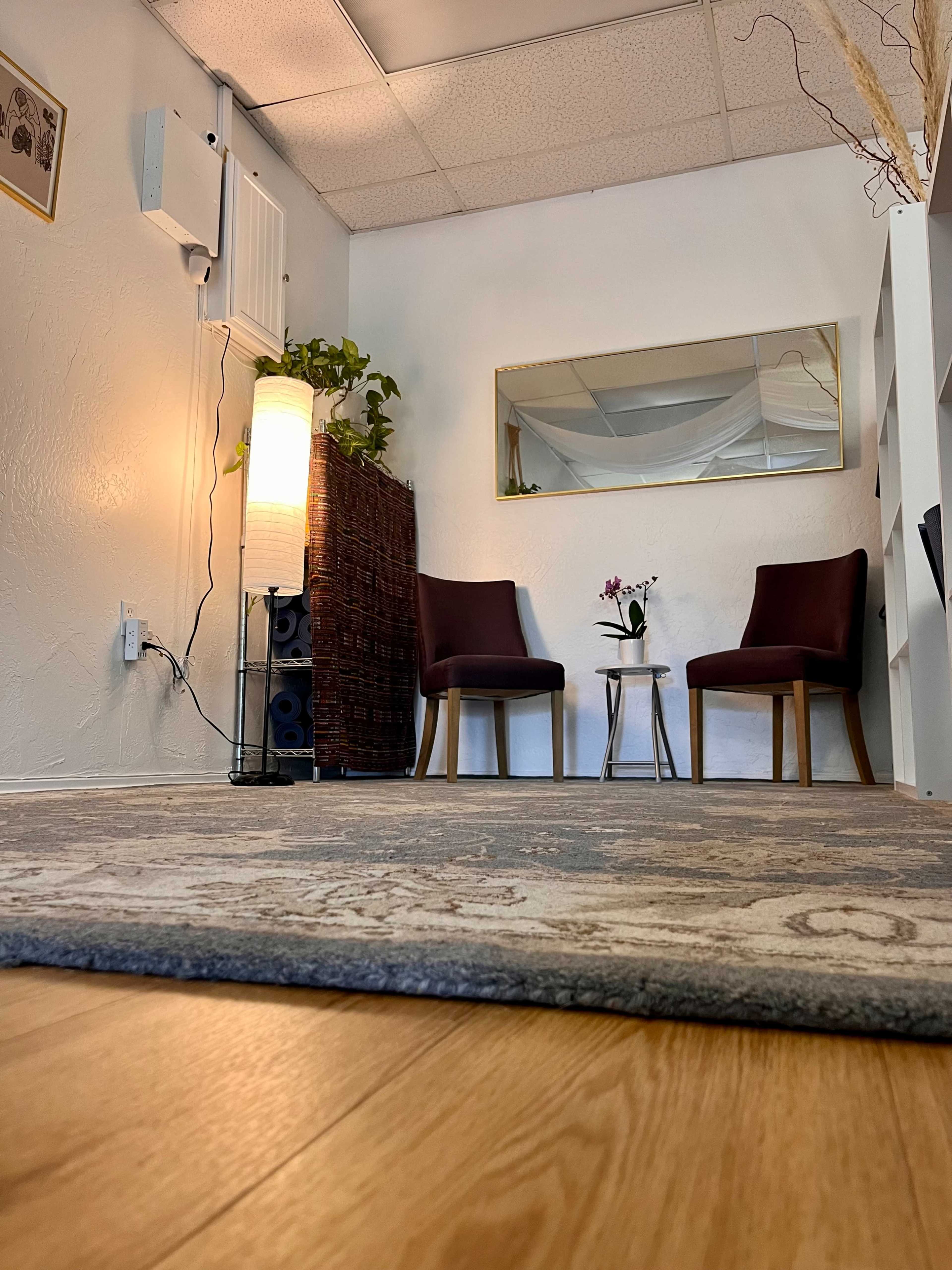 A small, well-lit room with two chairs, a table, a lamp, and a decorative rug.