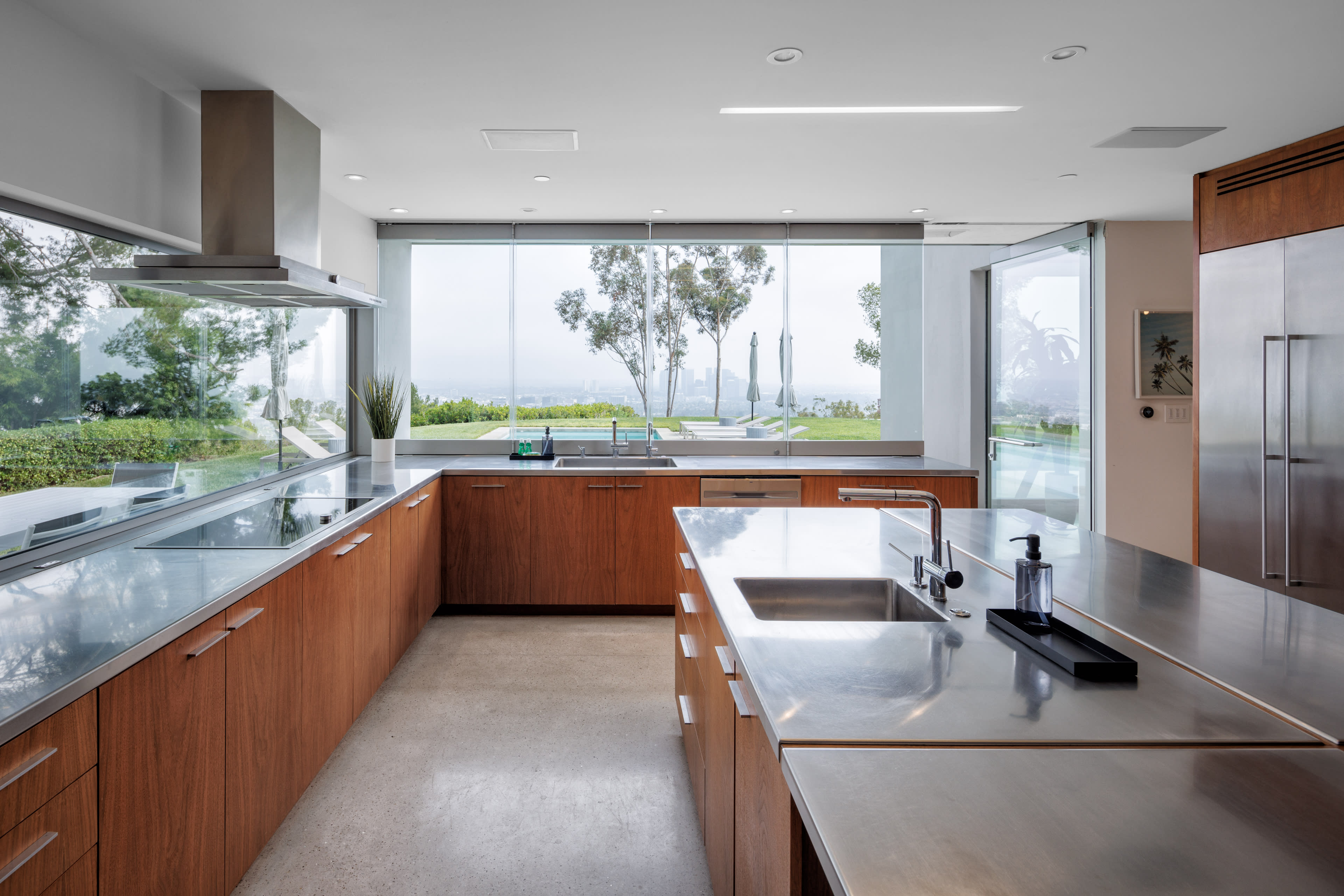 The modern kitchen features sleek stainless steel countertops, wooden cabinetry, and large windows that offer a view of the outdoors.