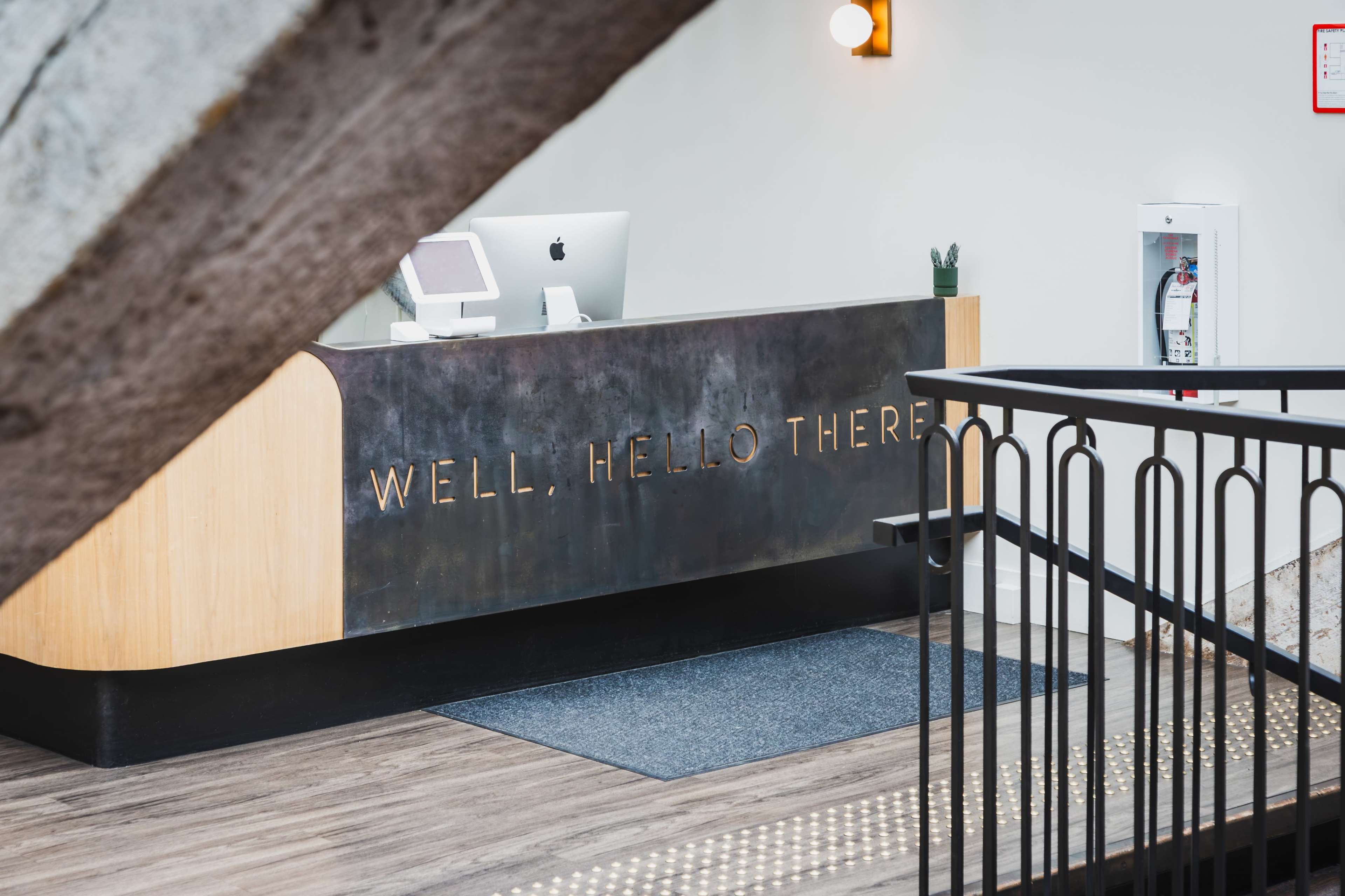 A reception desk is positioned at the entrance with a sign reading "WELL, HELLO THERE" and a computer setup.