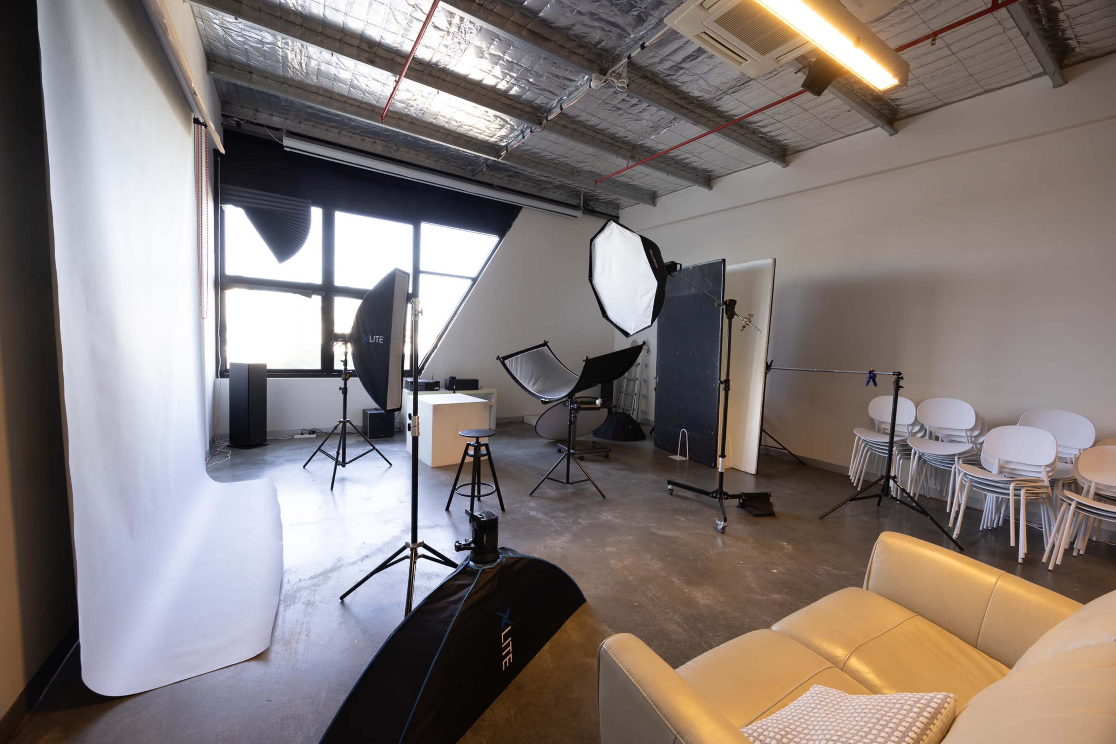 The image shows a photography studio equipped with various lighting setups, backdrops, and a seating area.