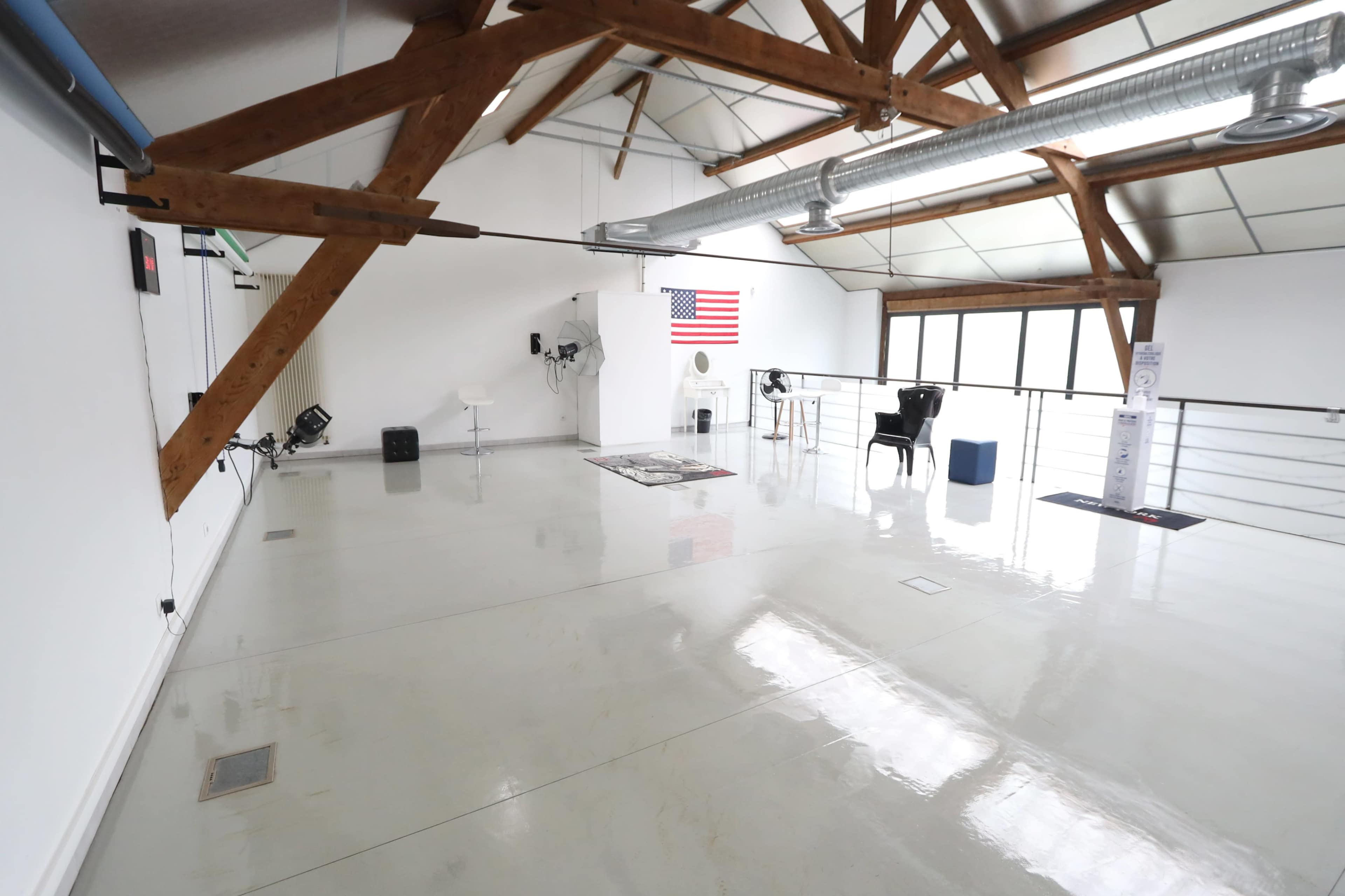 A spacious, well-lit room with wooden beams, a large American flag on the wall, and minimal furnishings.