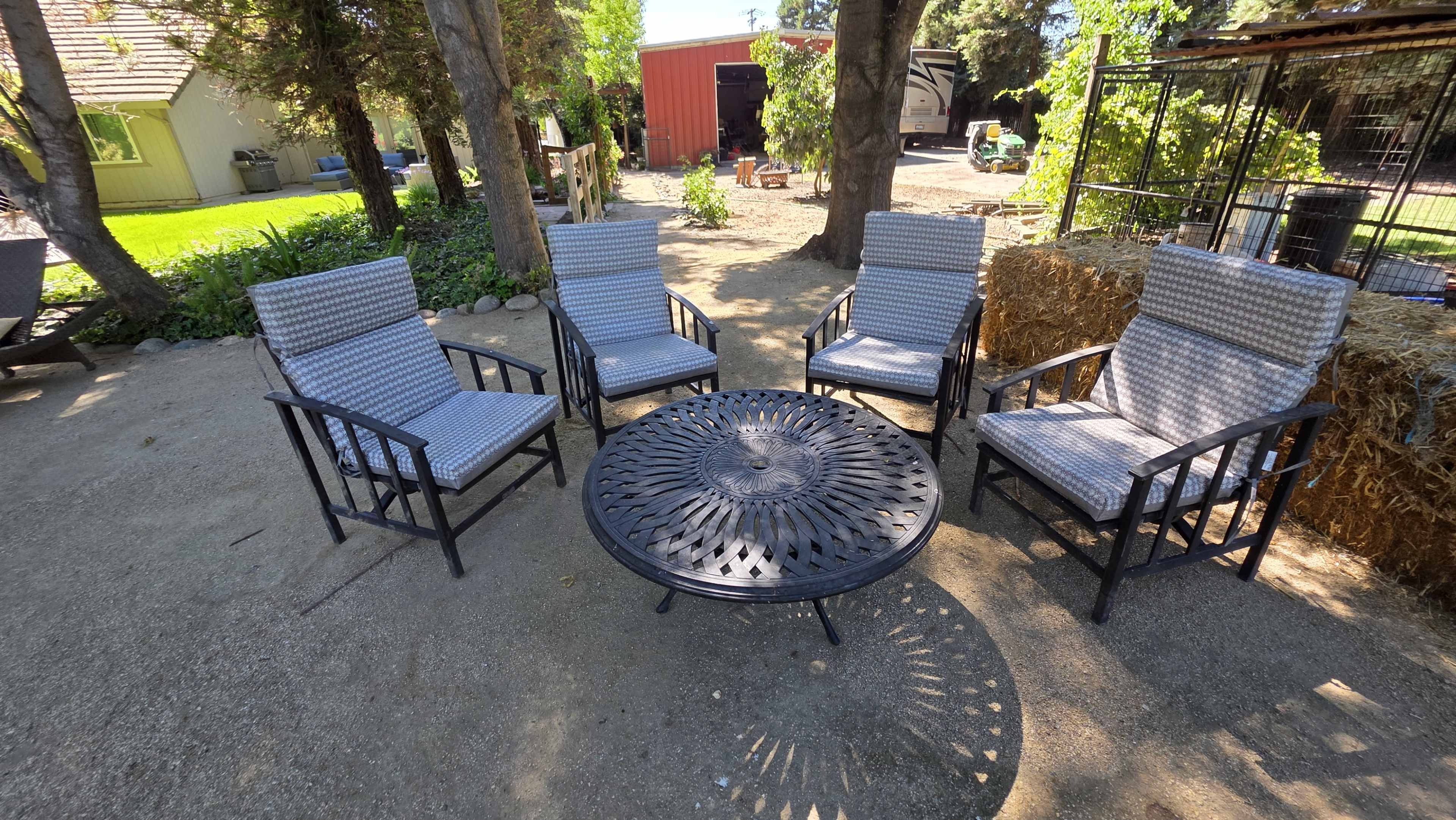 The image shows five outdoor chairs arranged around a circular metal table in a garden setting.