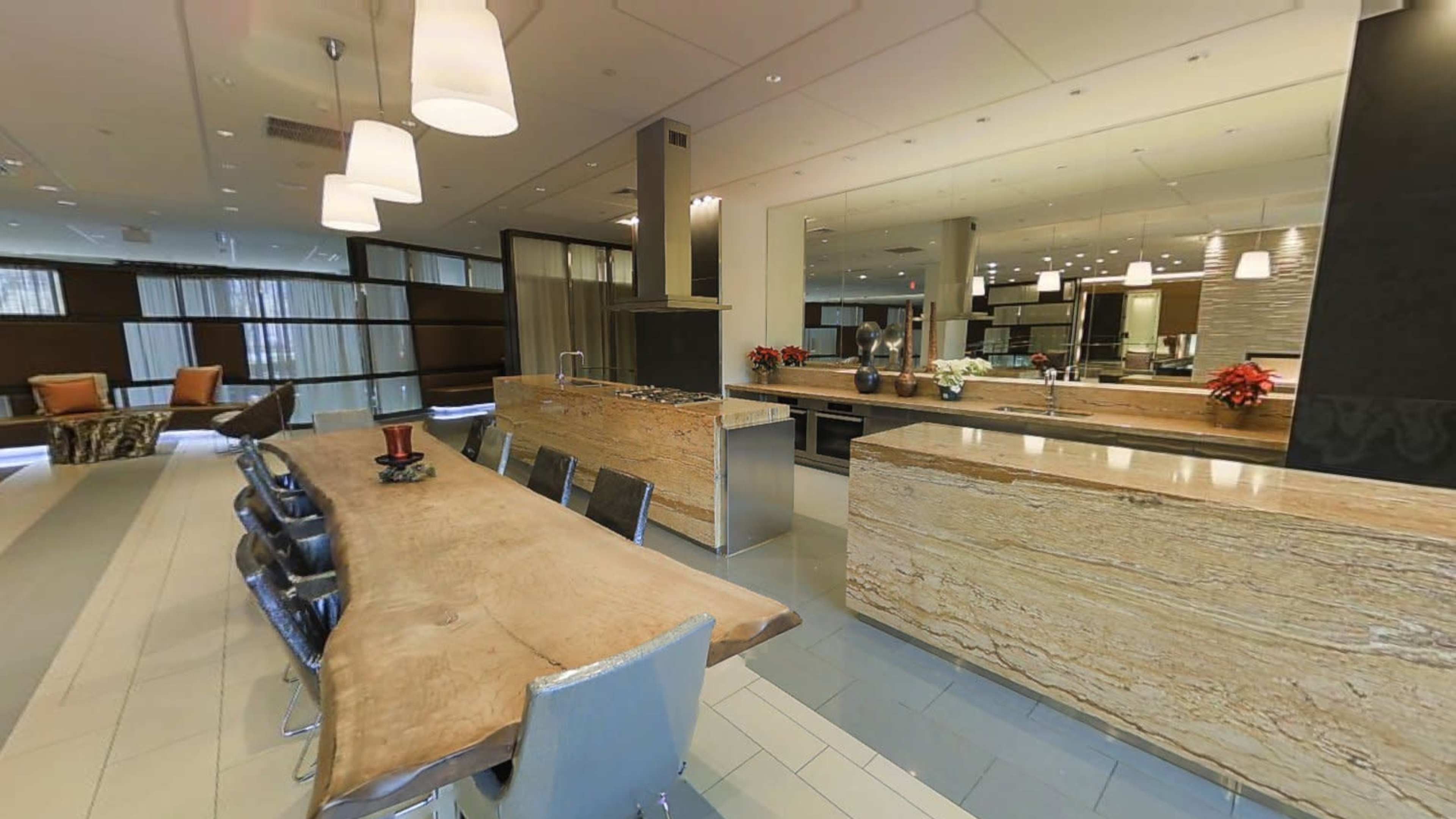 A modern kitchen and dining area featuring a large wooden table, granite countertops, and contemporary lighting fixtures.