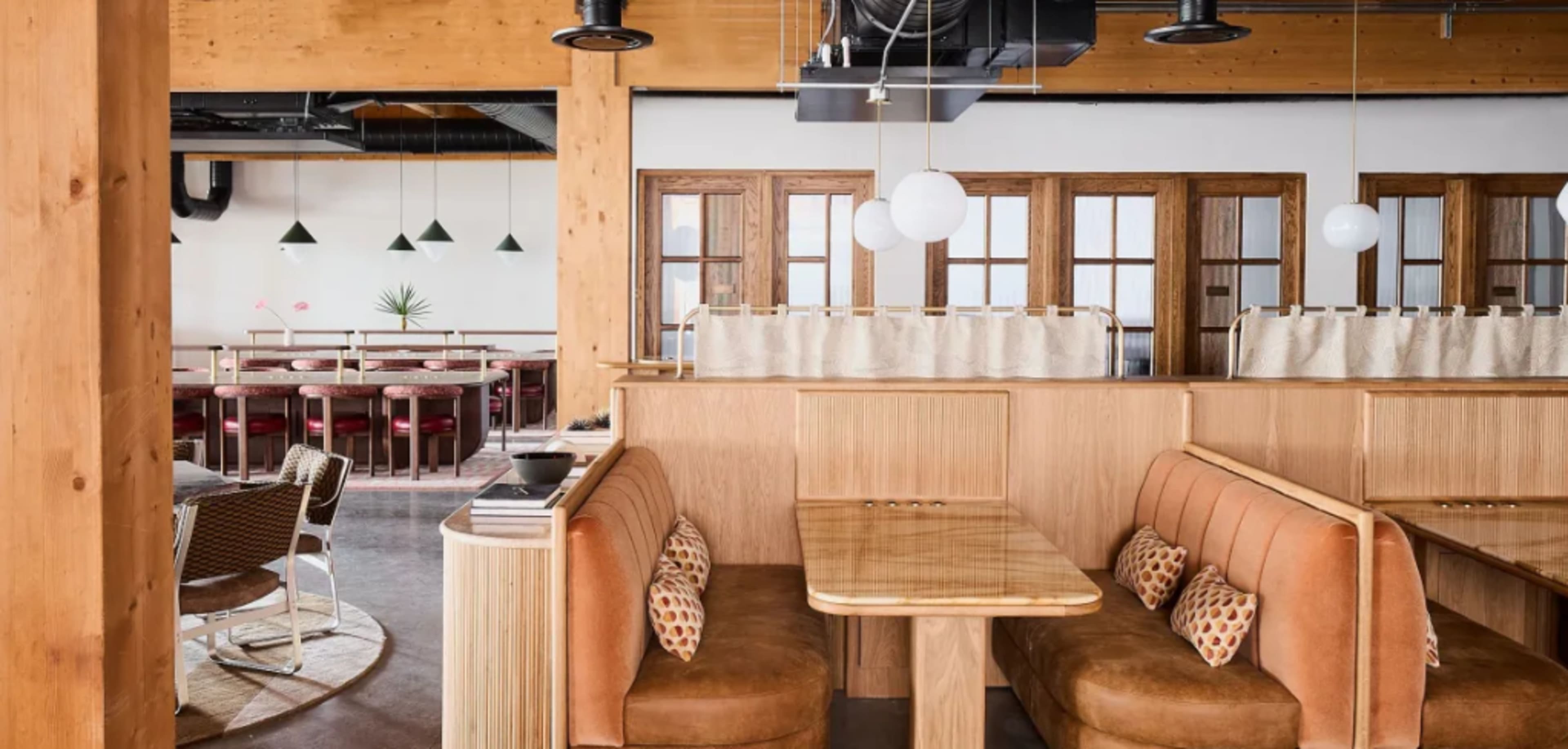 A modern restaurant interior featuring wooden partitions, upholstered booths, and a dining area with round tables and chairs.