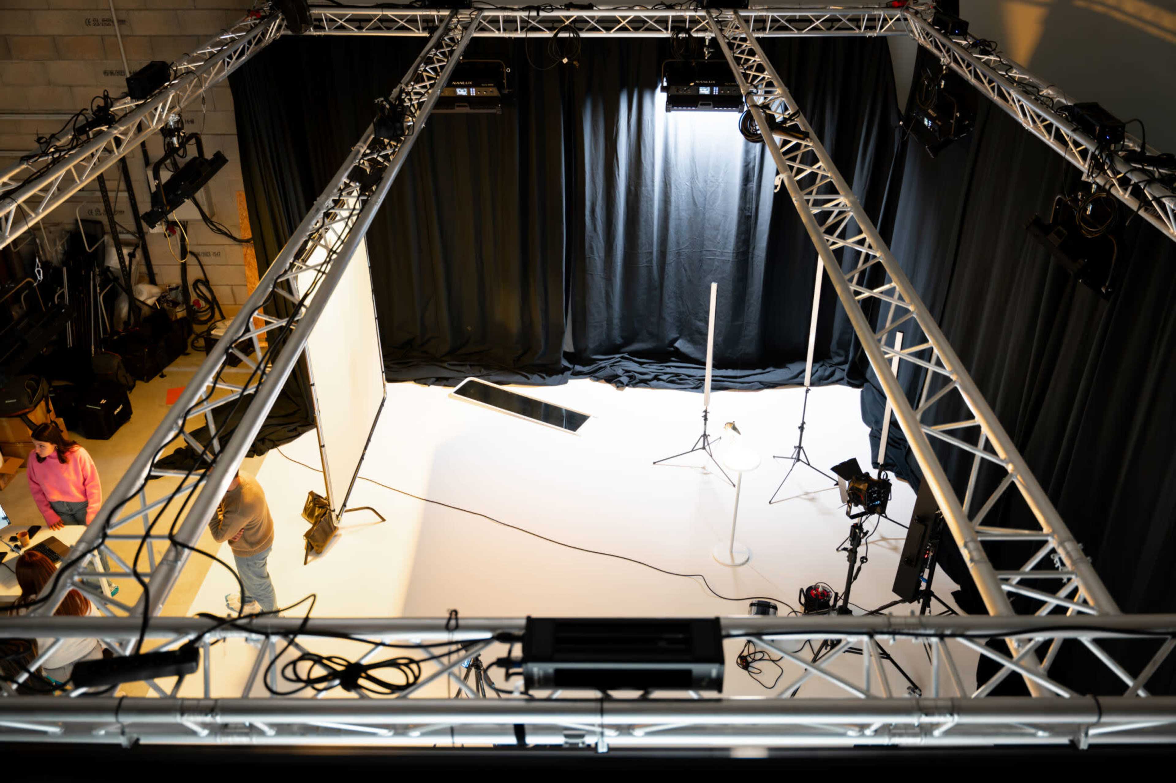 An overhead view of a photography studio with lighting rigs, black curtains, and a white backdrop.