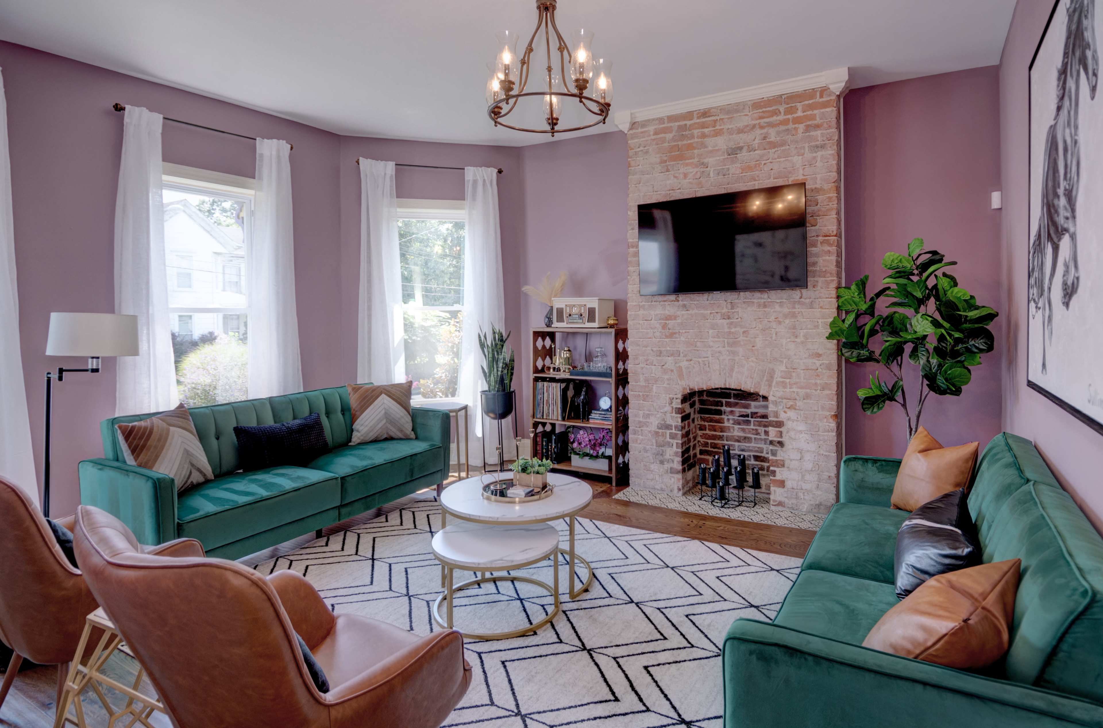 The living room features green sofas, a round coffee table, a brick fireplace, and large windows with white curtains.