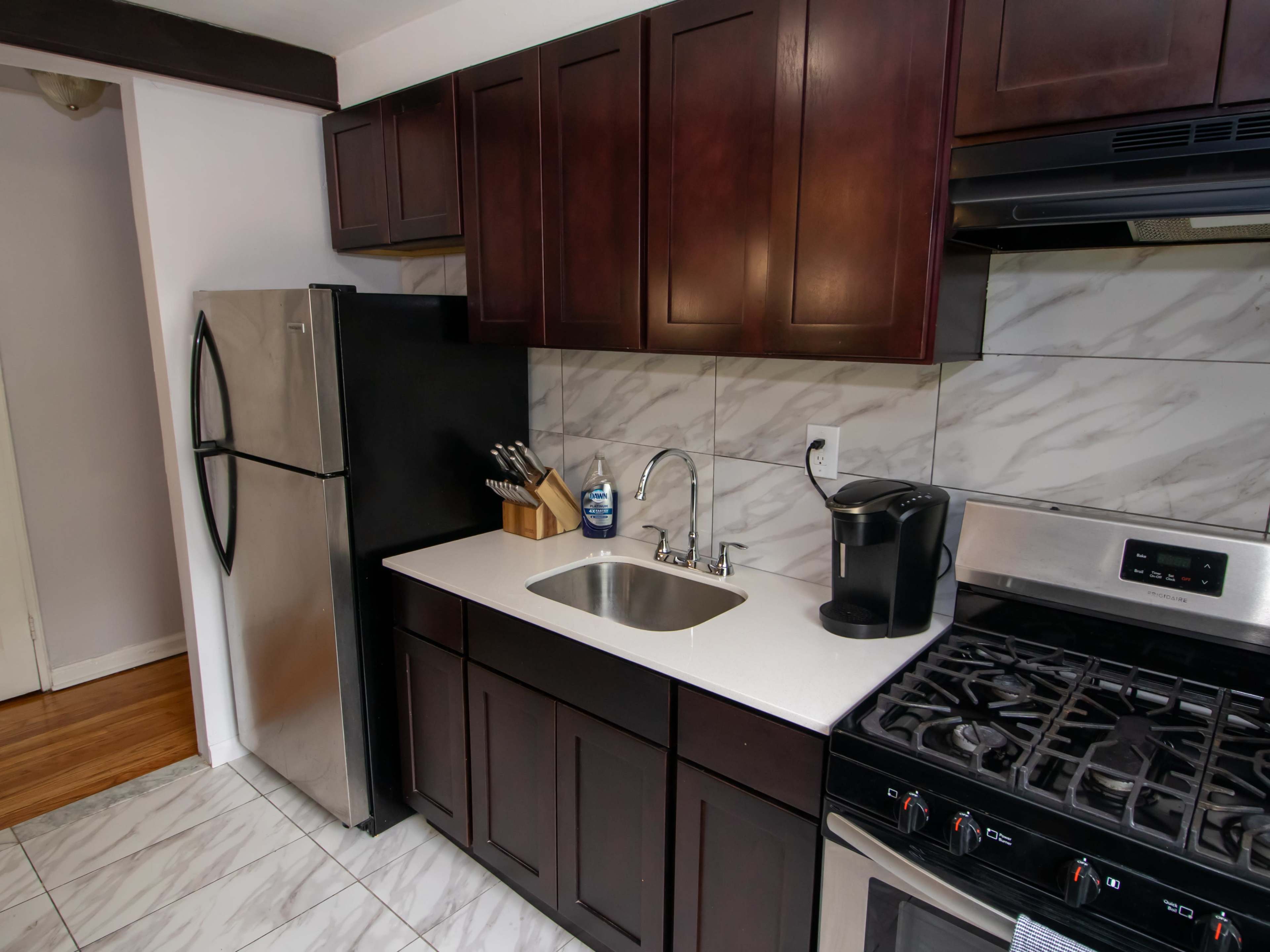 The image shows a modern kitchen featuring dark cabinetry, stainless steel appliances, a marble backsplash, and a gas stove.