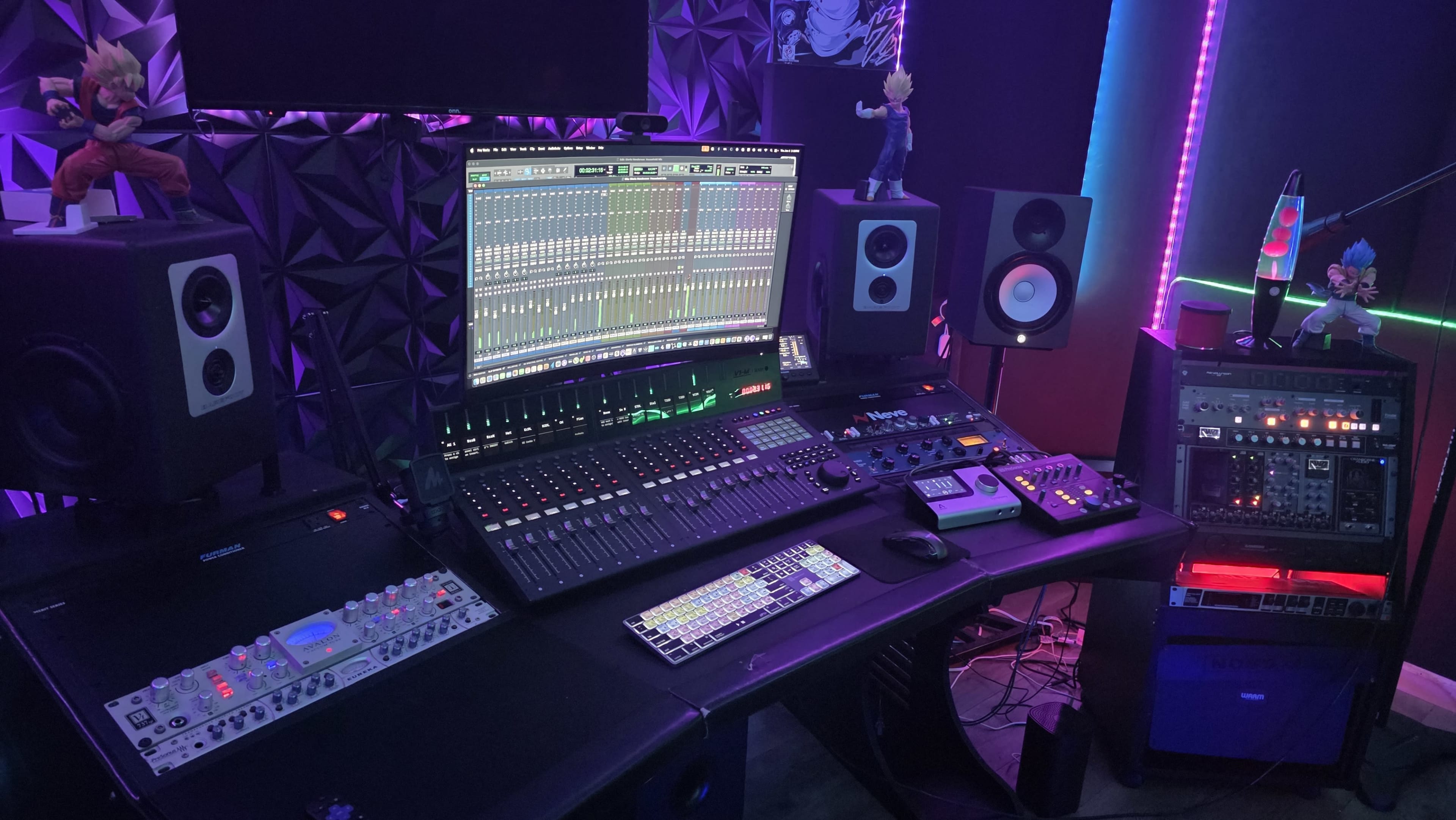 A digital audio workstation setup features a large mixing console, multiple speakers, and various sound equipment, with colorful LED lights and figurines as decor.