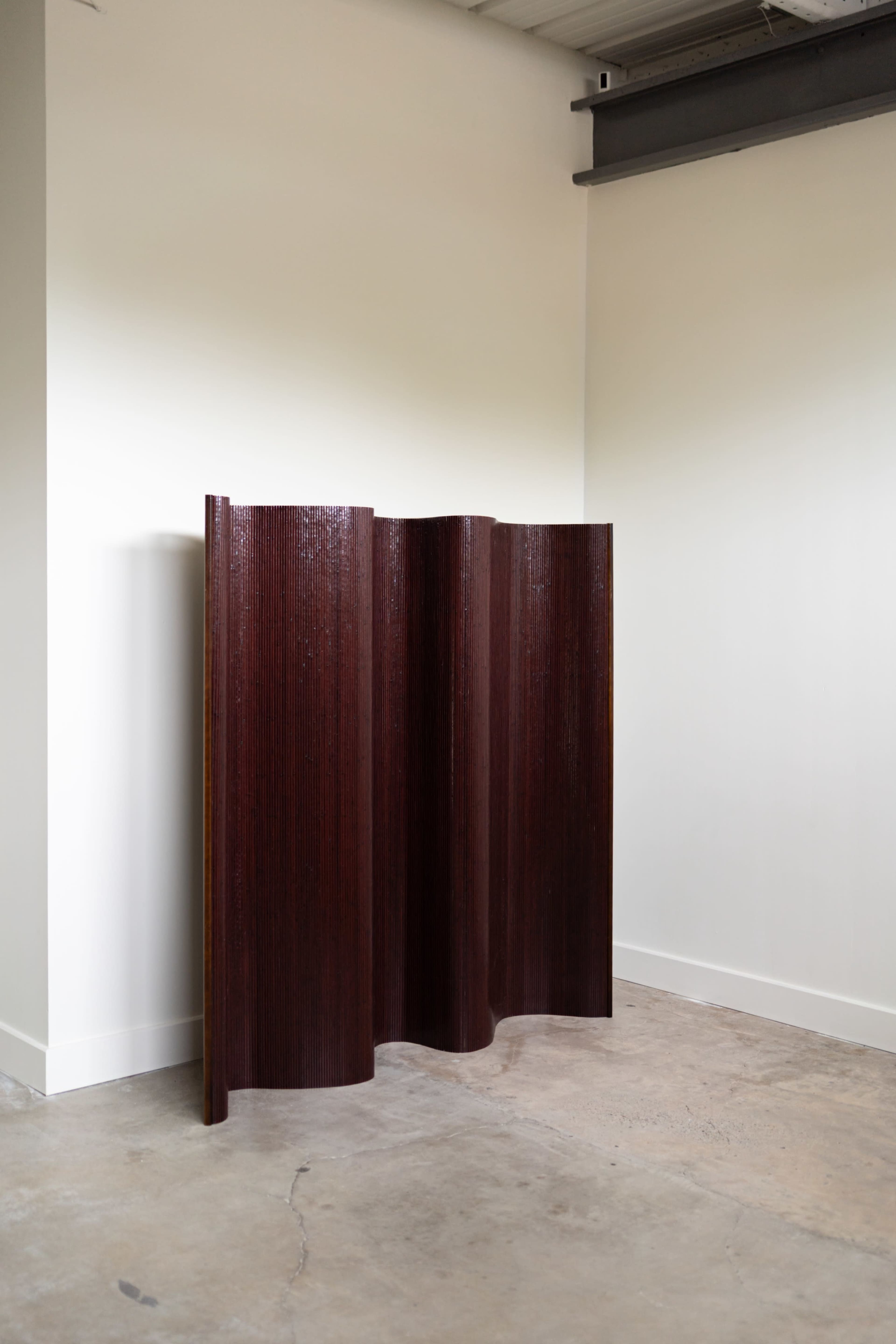 A three-panel folding screen with a textured, dark wood finish stands in a minimalist interior space.