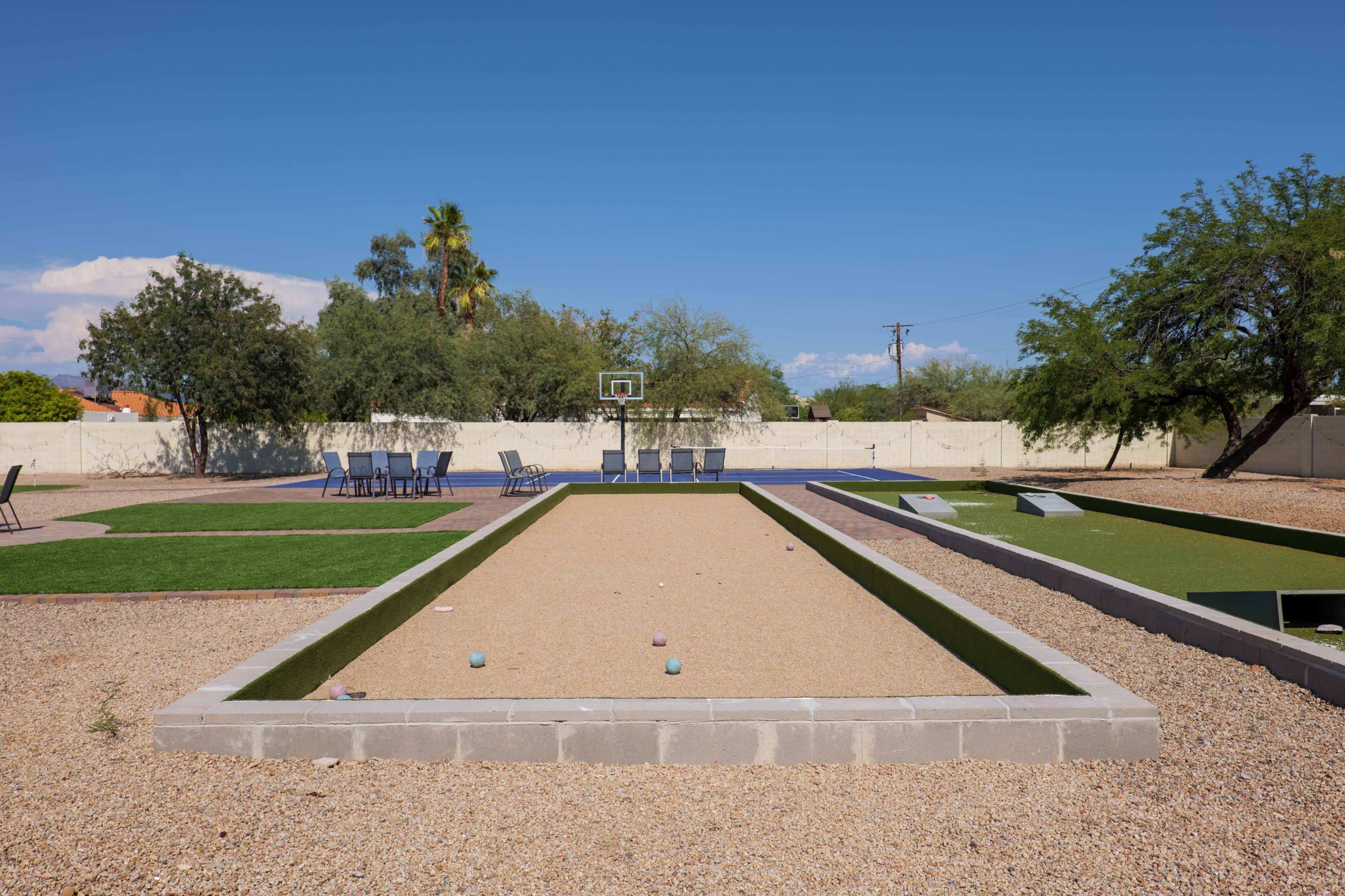 The image shows a bocce ball court surrounded by seating areas and greenery under a clear blue sky.